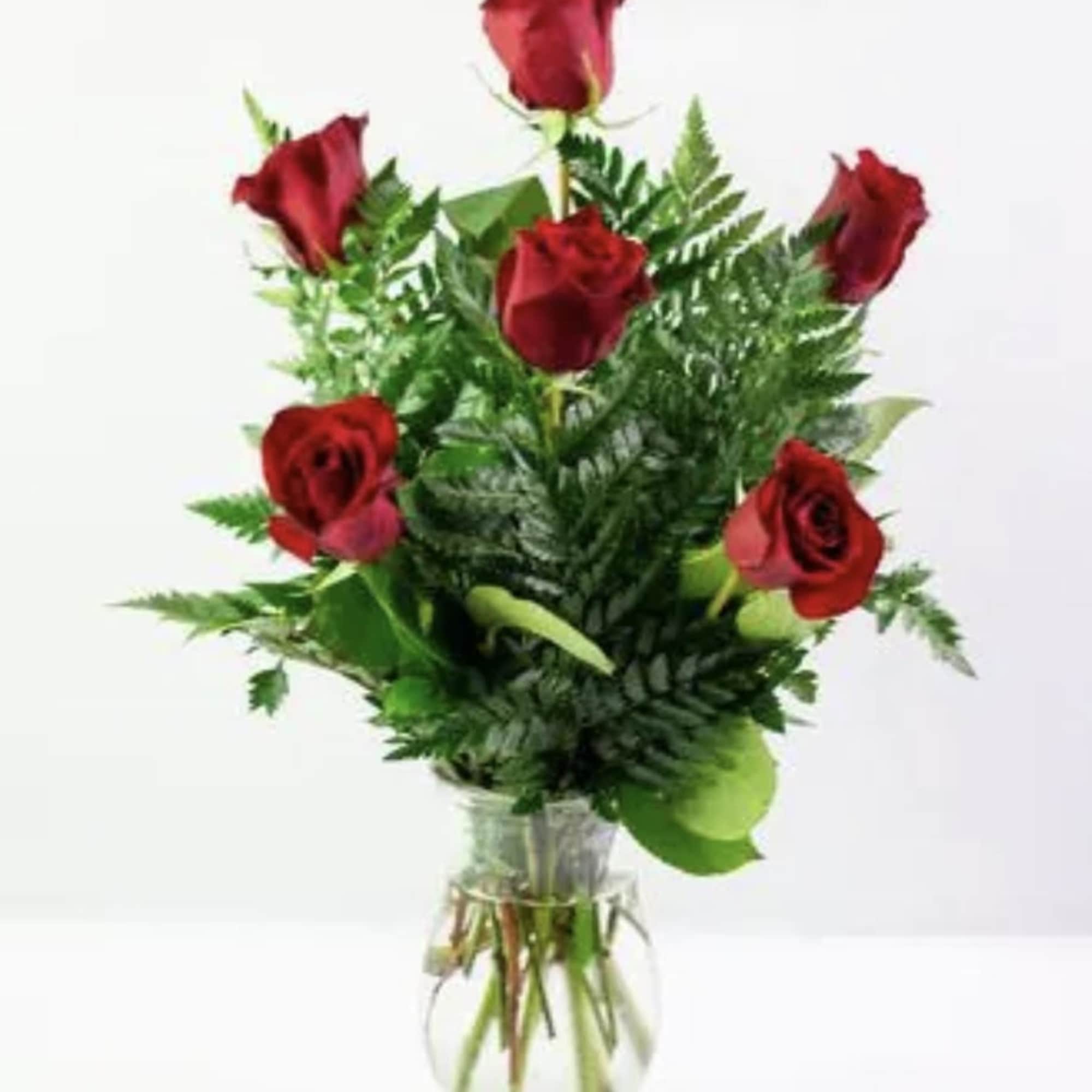 Five red roses in a clear glass vase with fern foliage