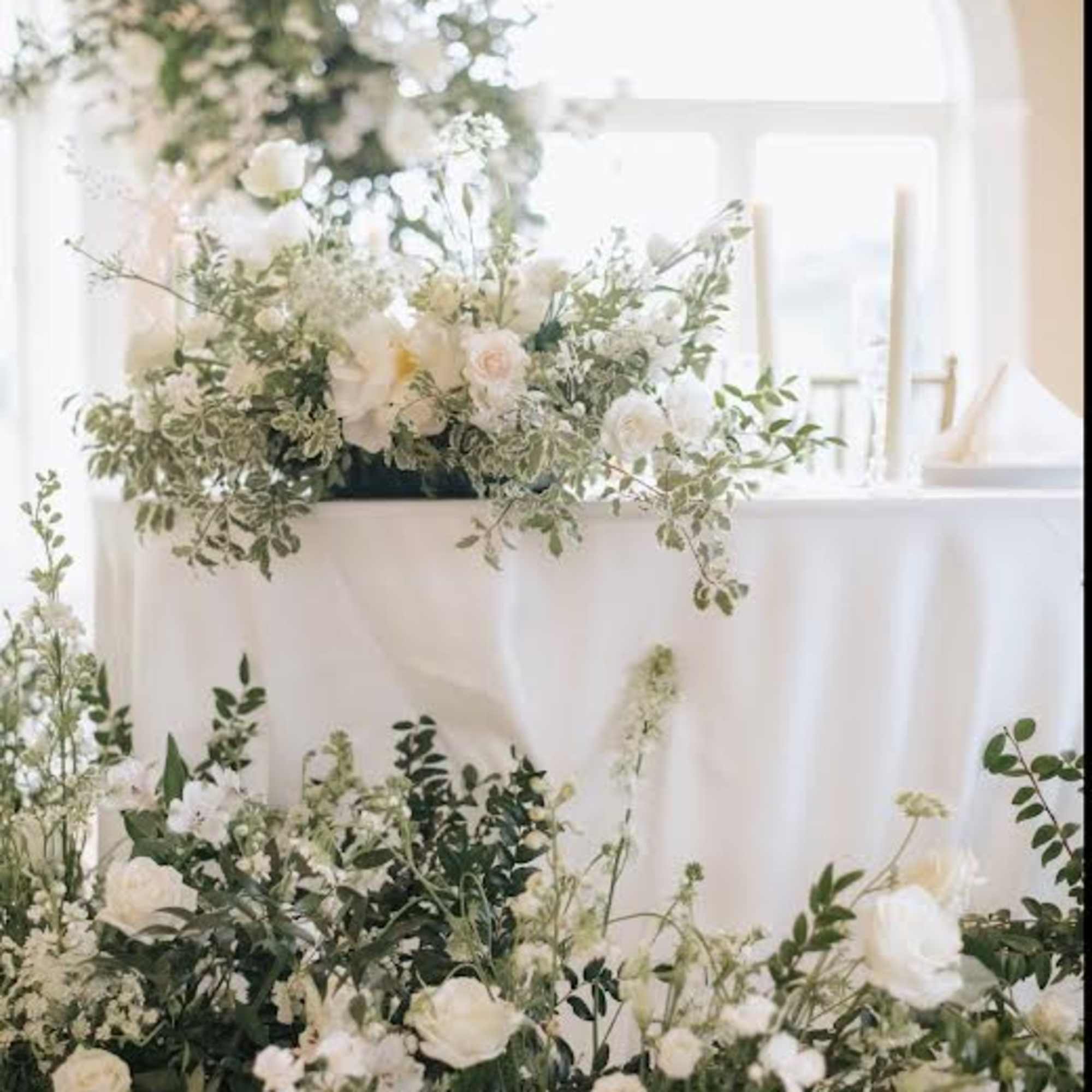 White floral arrangements with greenery on a draped table in a bright room