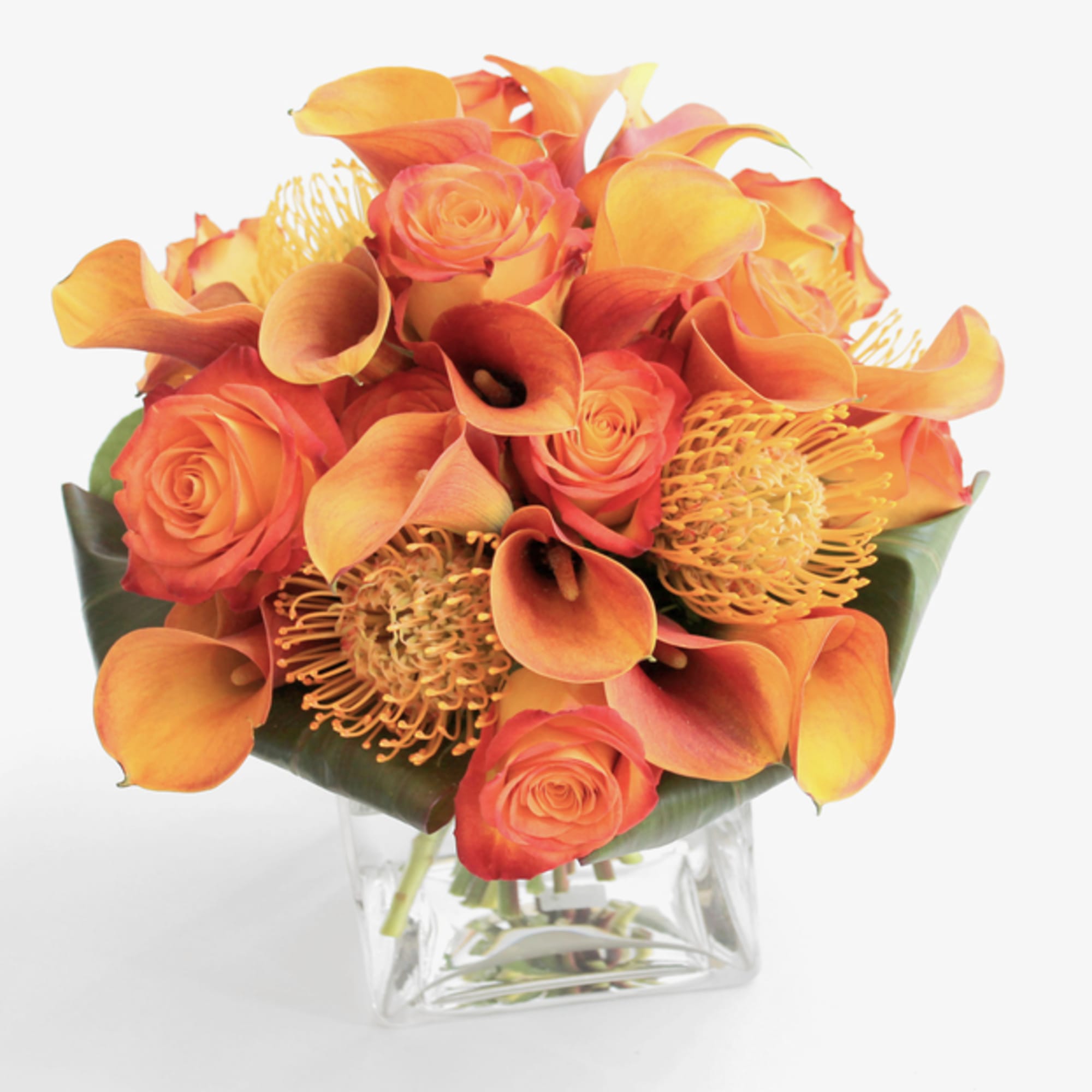 Orange roses and calla lilies in a clear glass vase