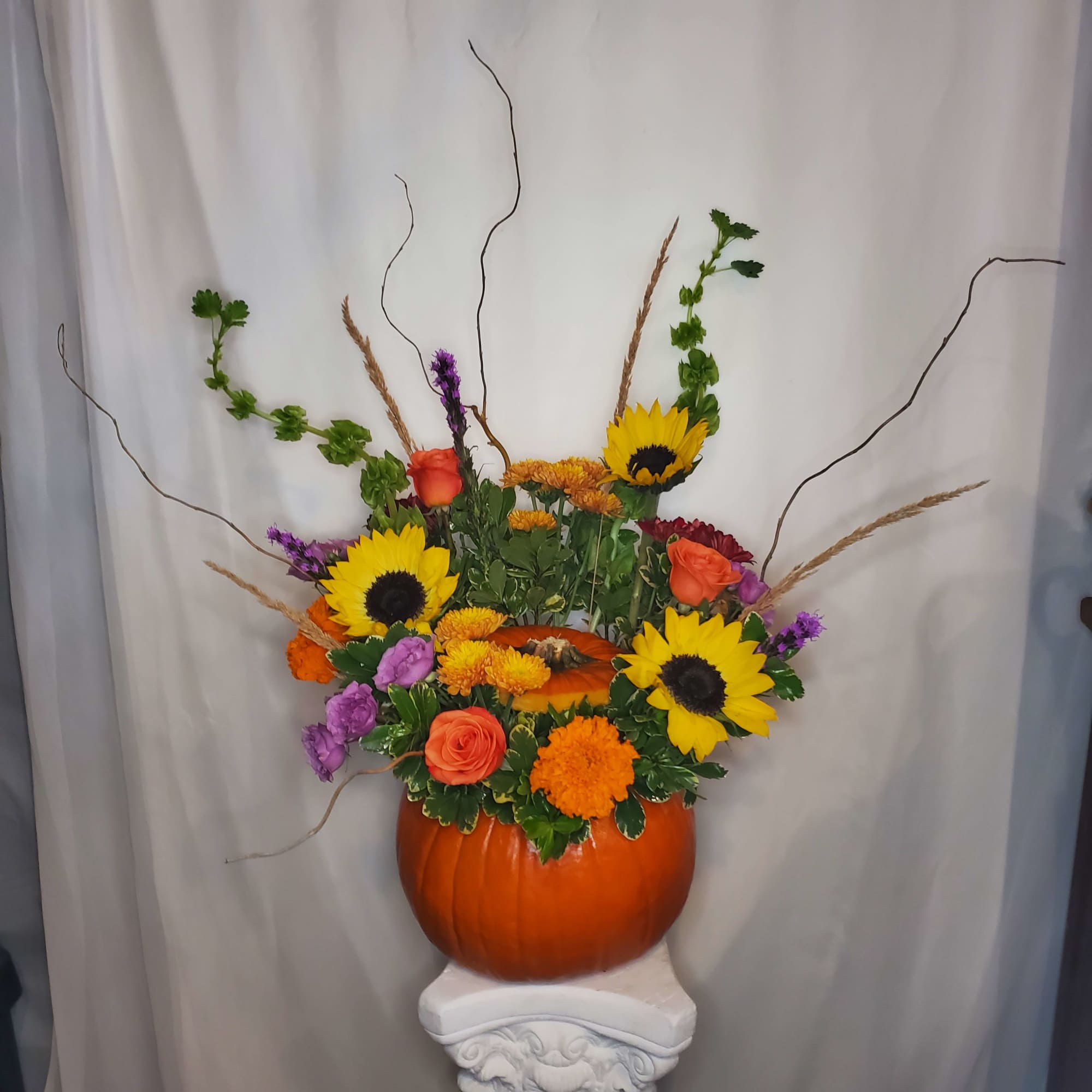 Pumpkin vase arrangement with sunflowers, roses, and purple blooms