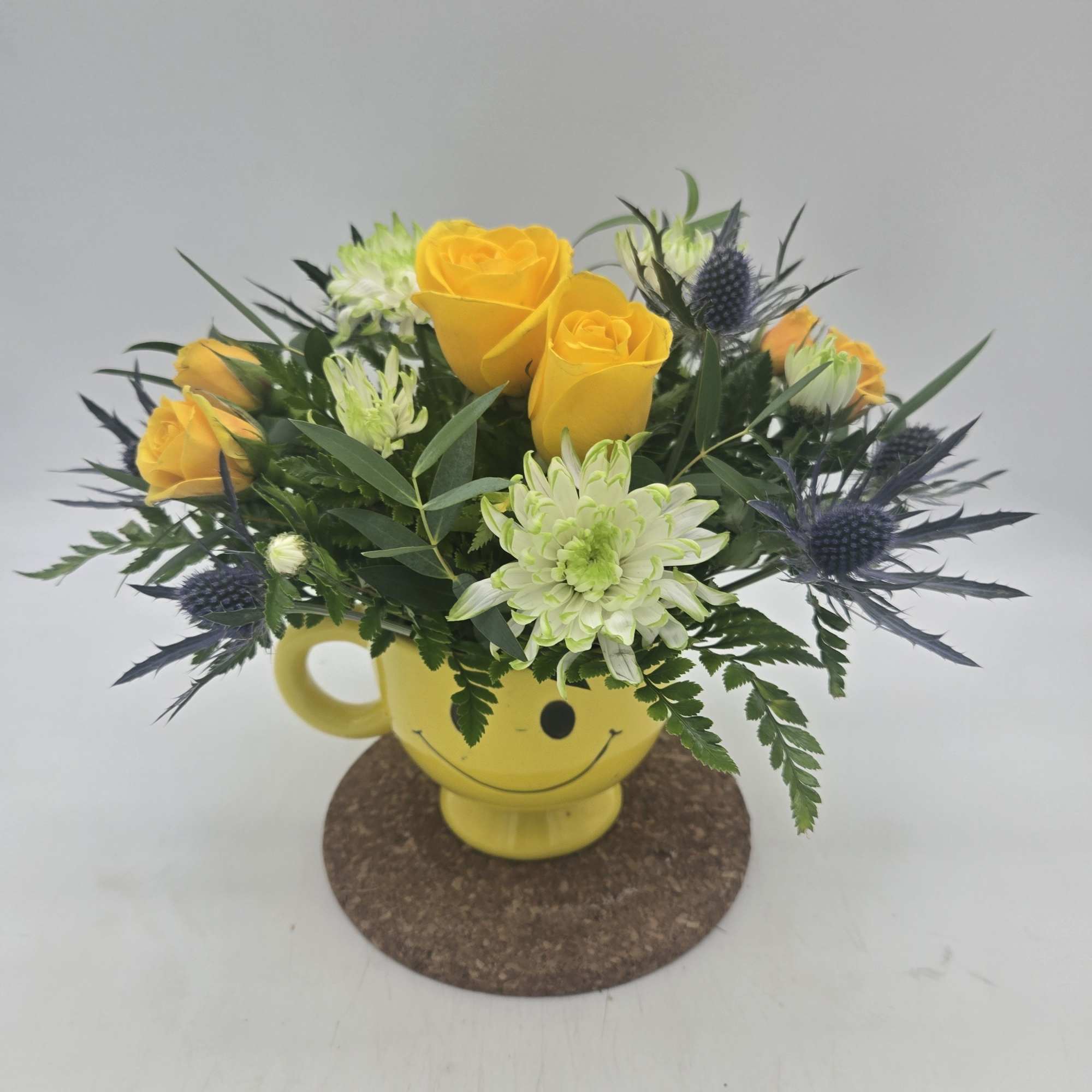 Yellow roses and pale green chrysanthemums in a smiley-face mug