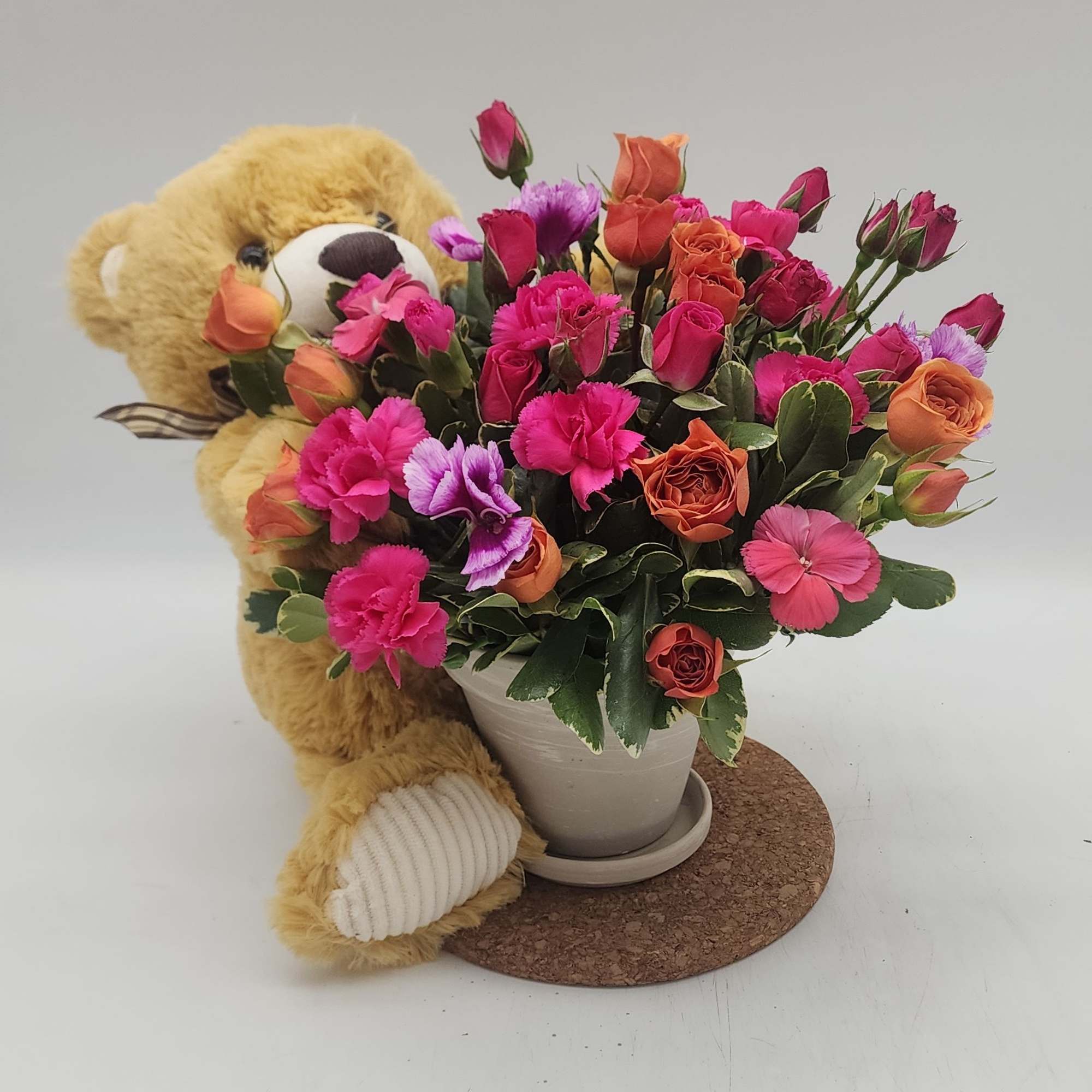 Teddy bear beside a mixed bouquet in a white pot