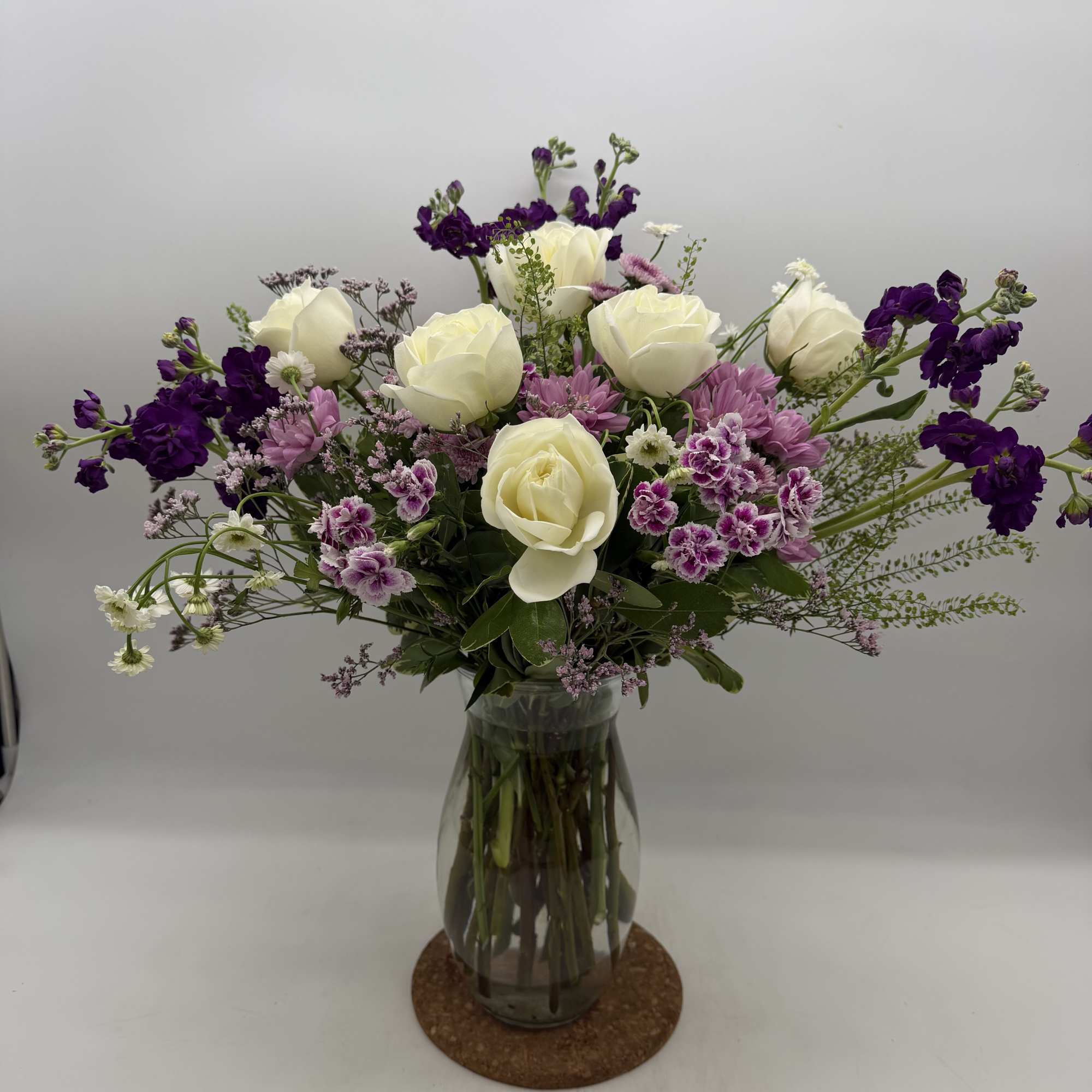 Creamy white roses mingle with lavender-hued stock and purple alstroemeria in a