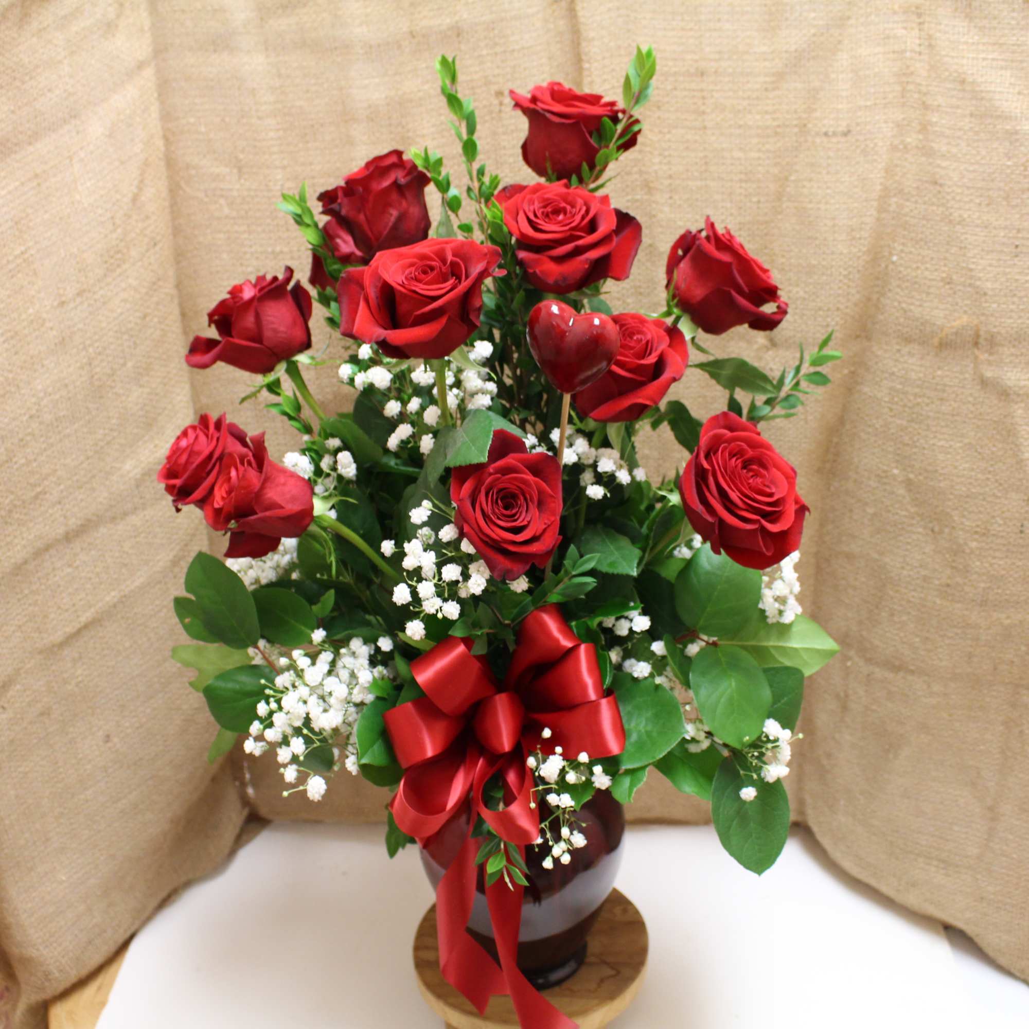 Red roses arranged in a vase with baby's breath and a red ribbon