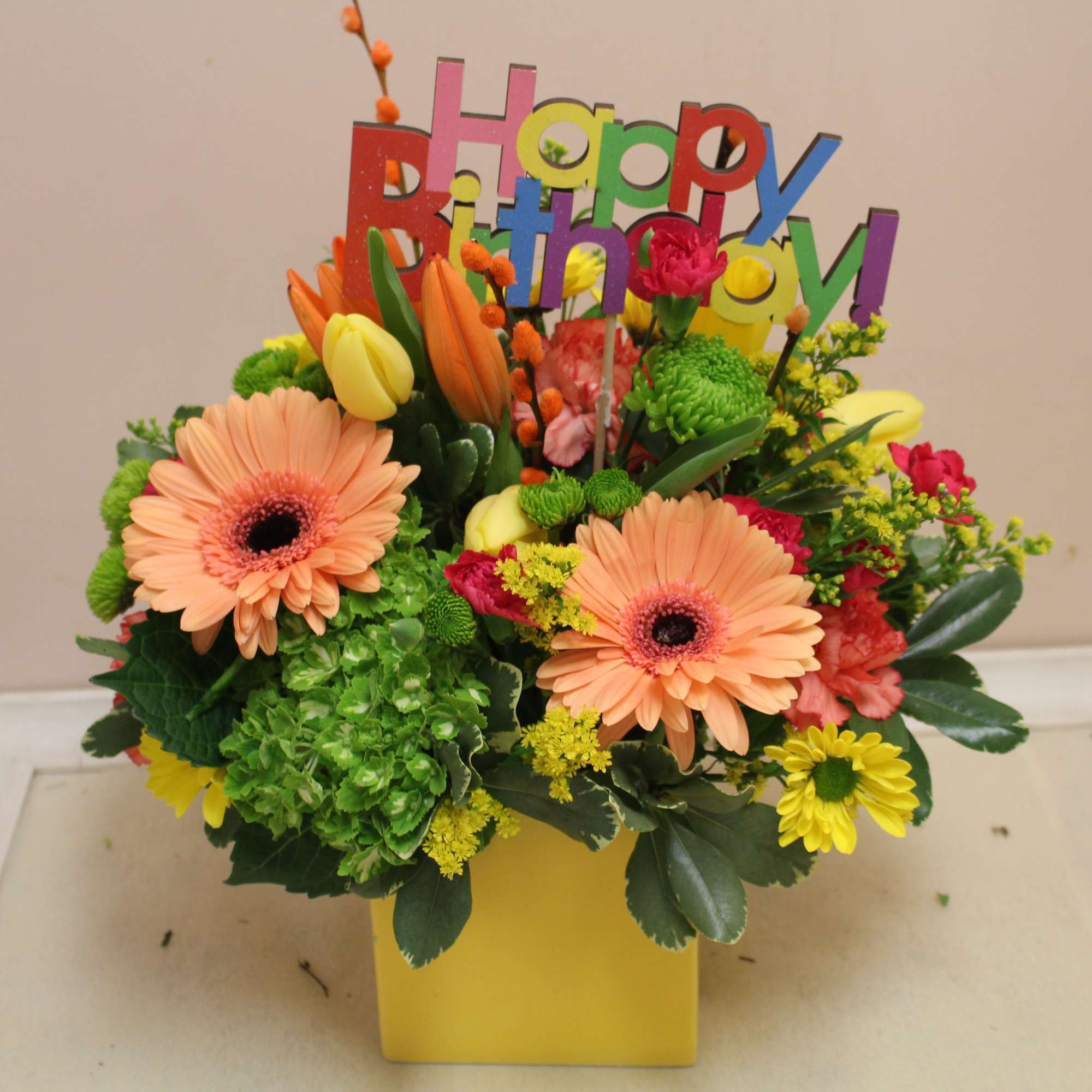 Colorful birthday flower arrangement with a "Happy Birthday" topper in a yellow vase