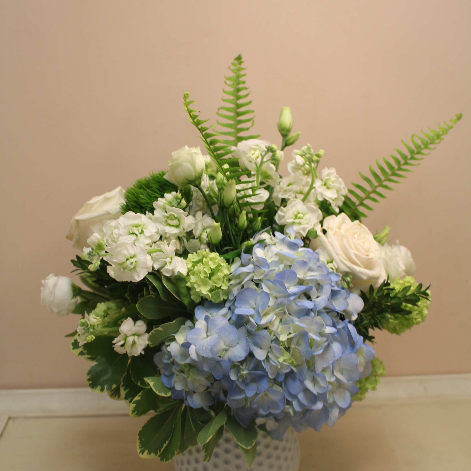 Blue hydrangea and white rose arrangement in a white textured vase