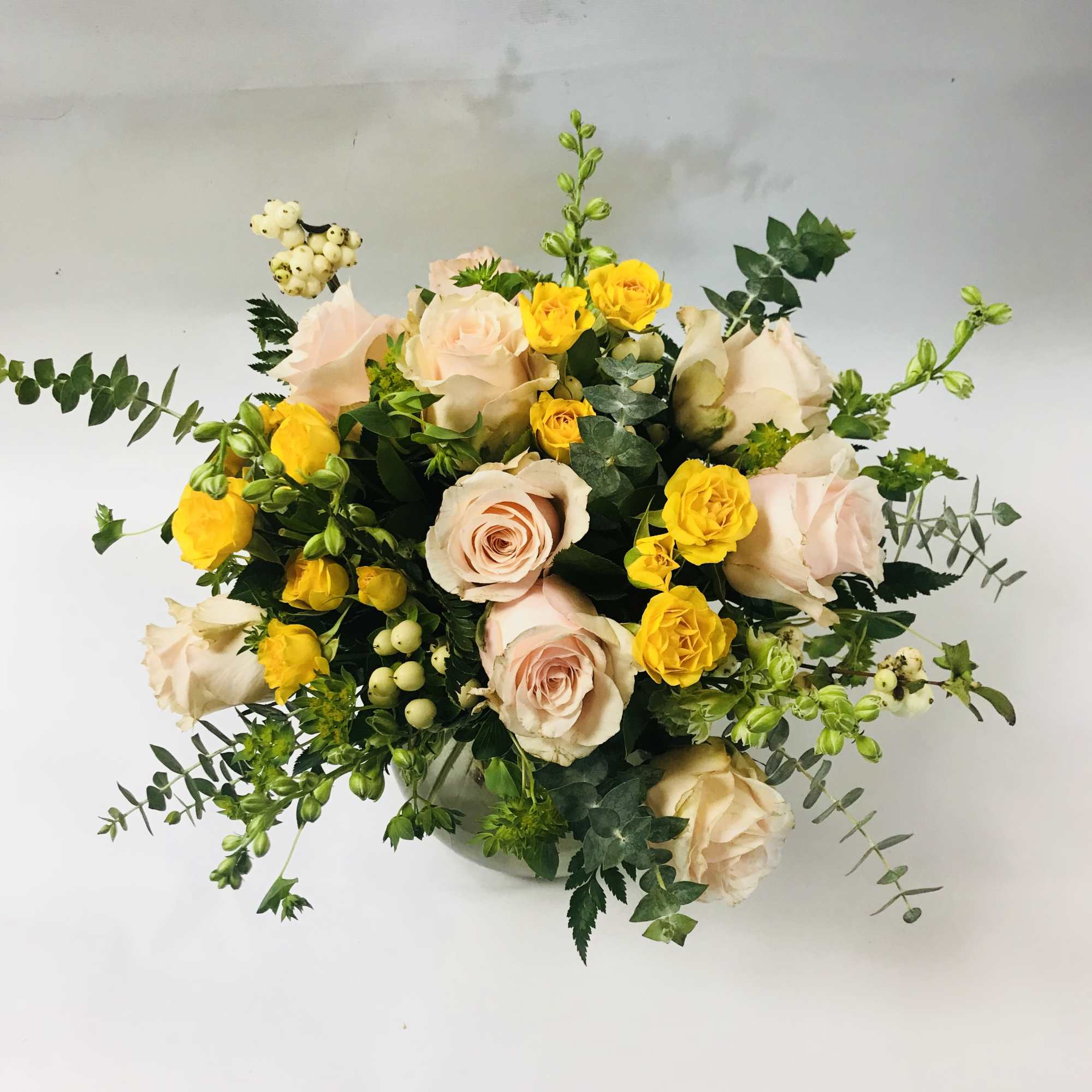 Bouquet of pale pink and yellow roses with greenery in a glass vase