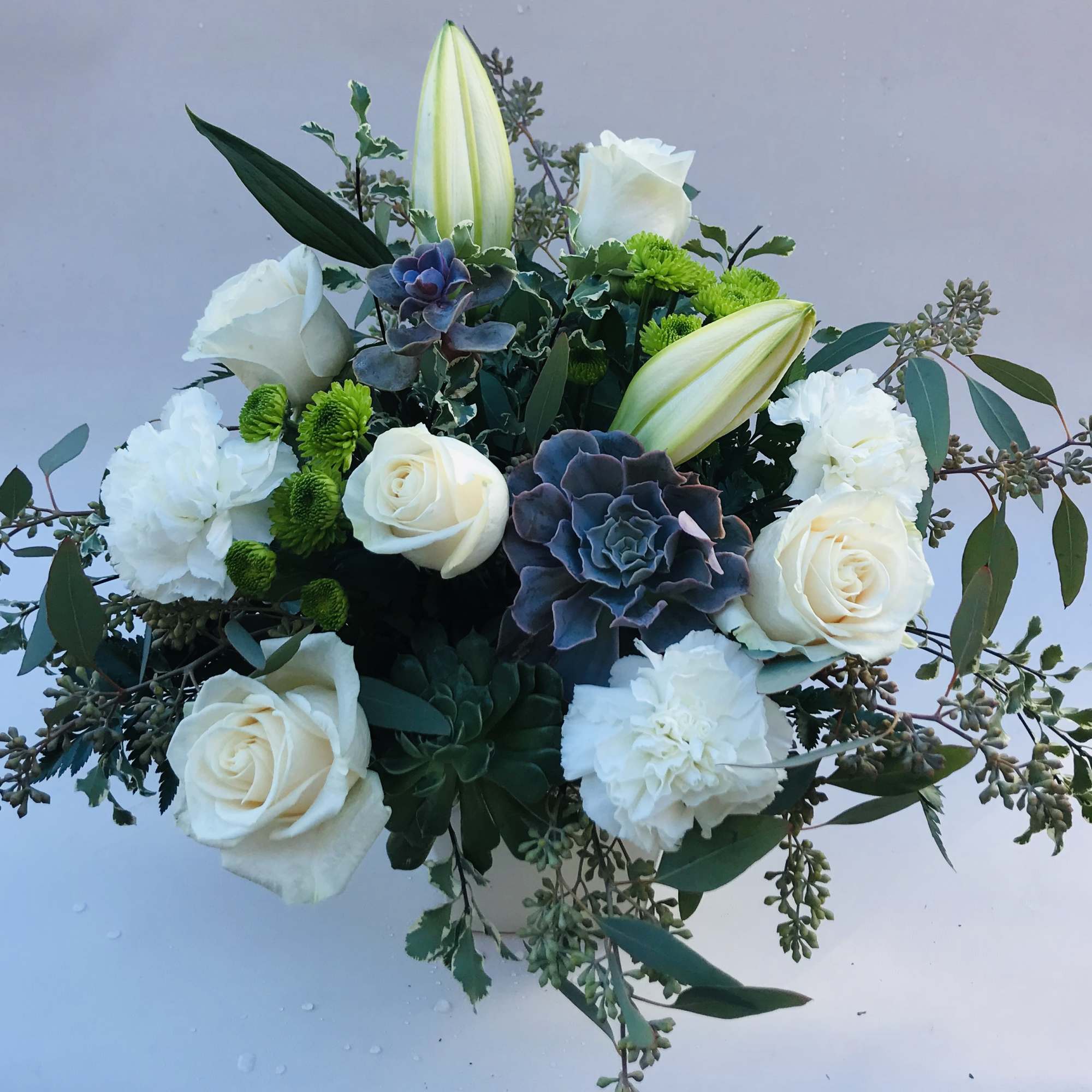 White roses and lilies arranged with succulents and greenery