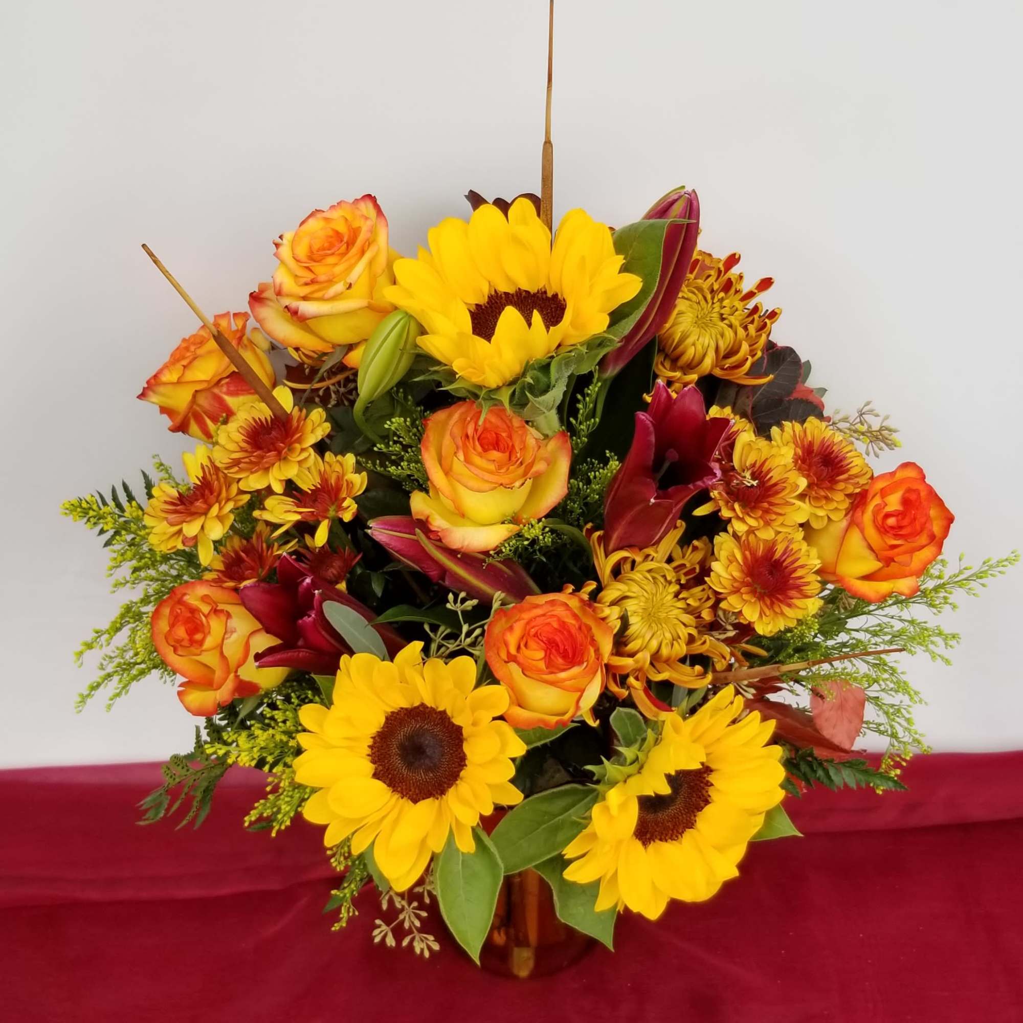 Bouquet of sunflowers, orange roses, and burgundy lilies in a vase