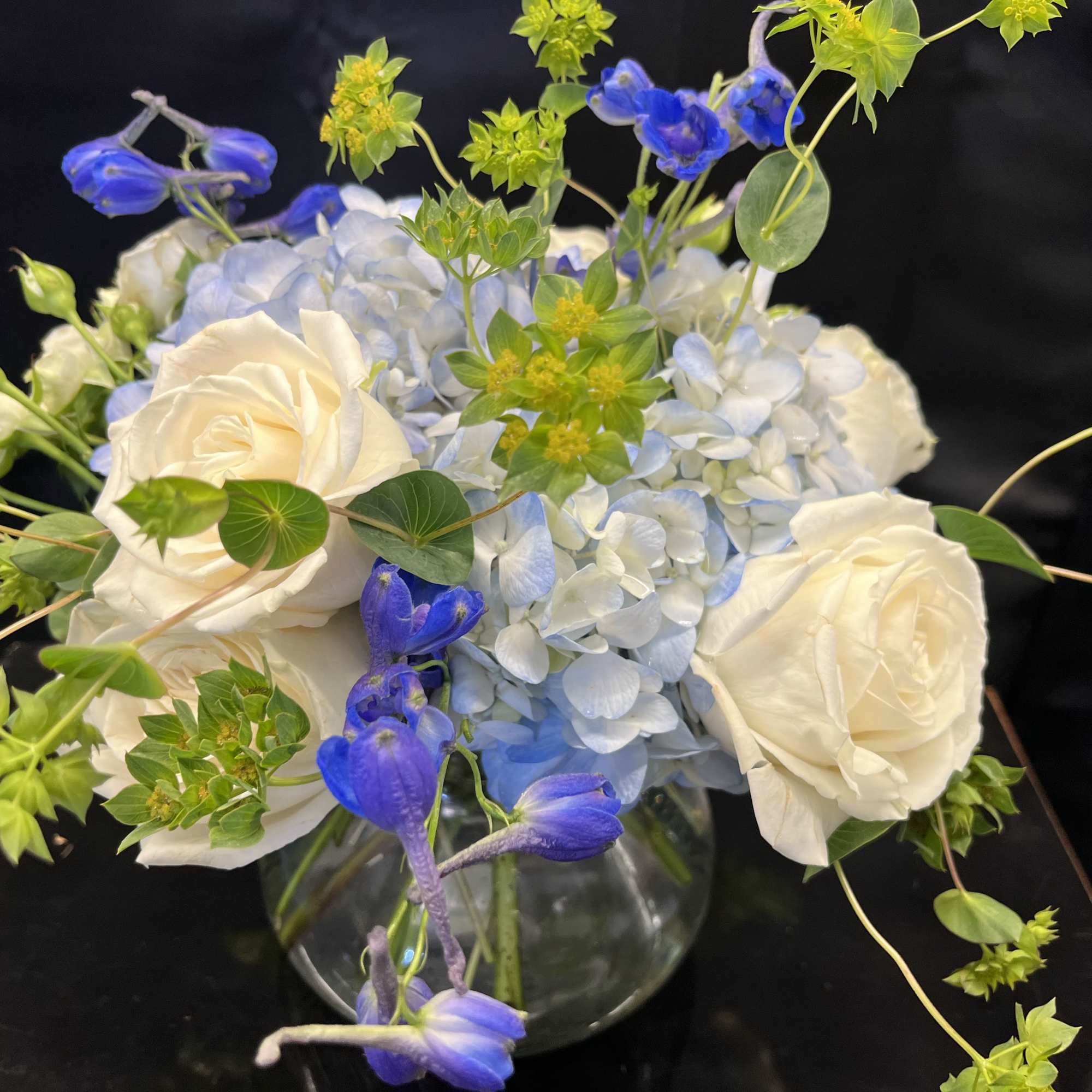 White roses and blue hydrangea in a glass vase with blue flowers