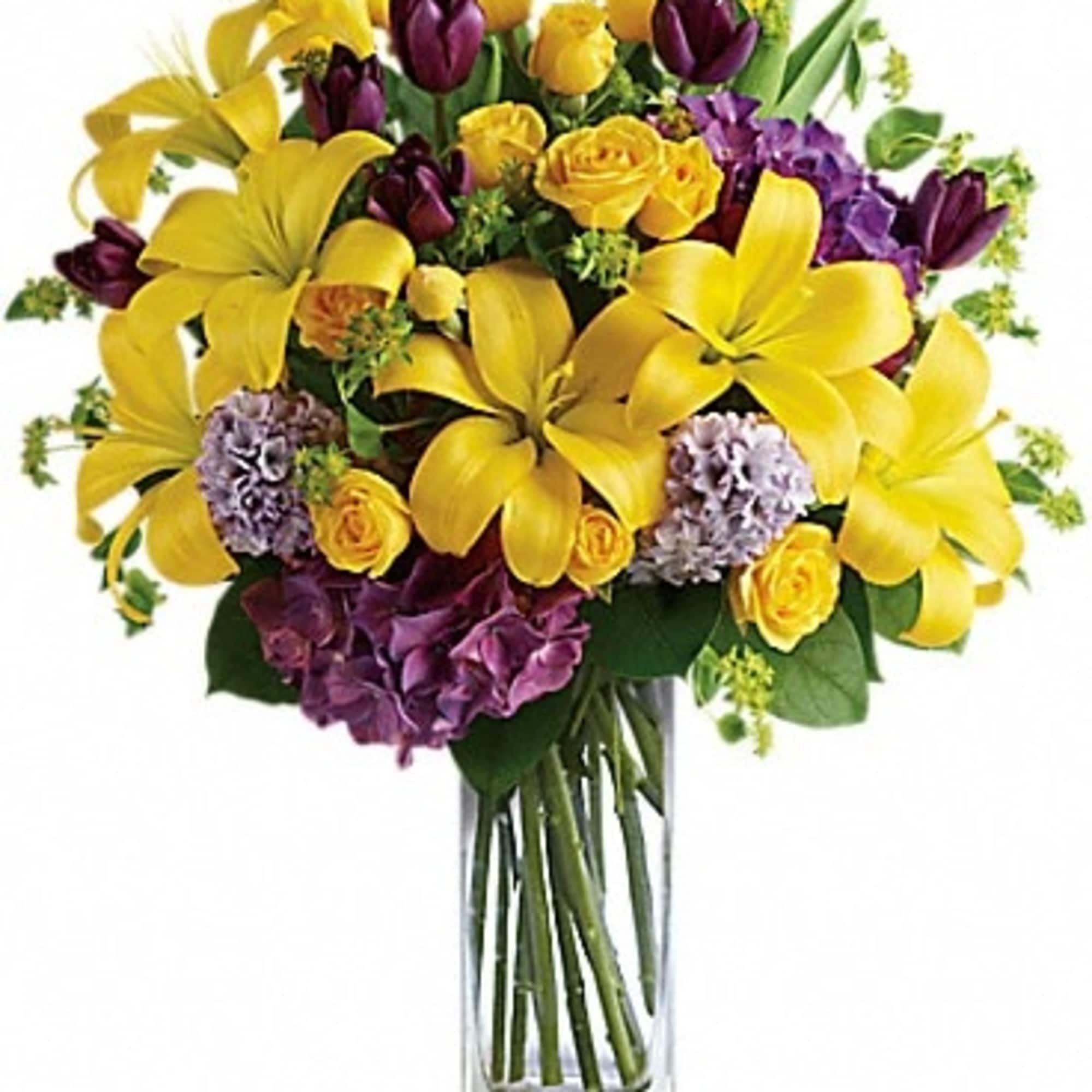Yellow lilies and purple flowers in a clear glass vase