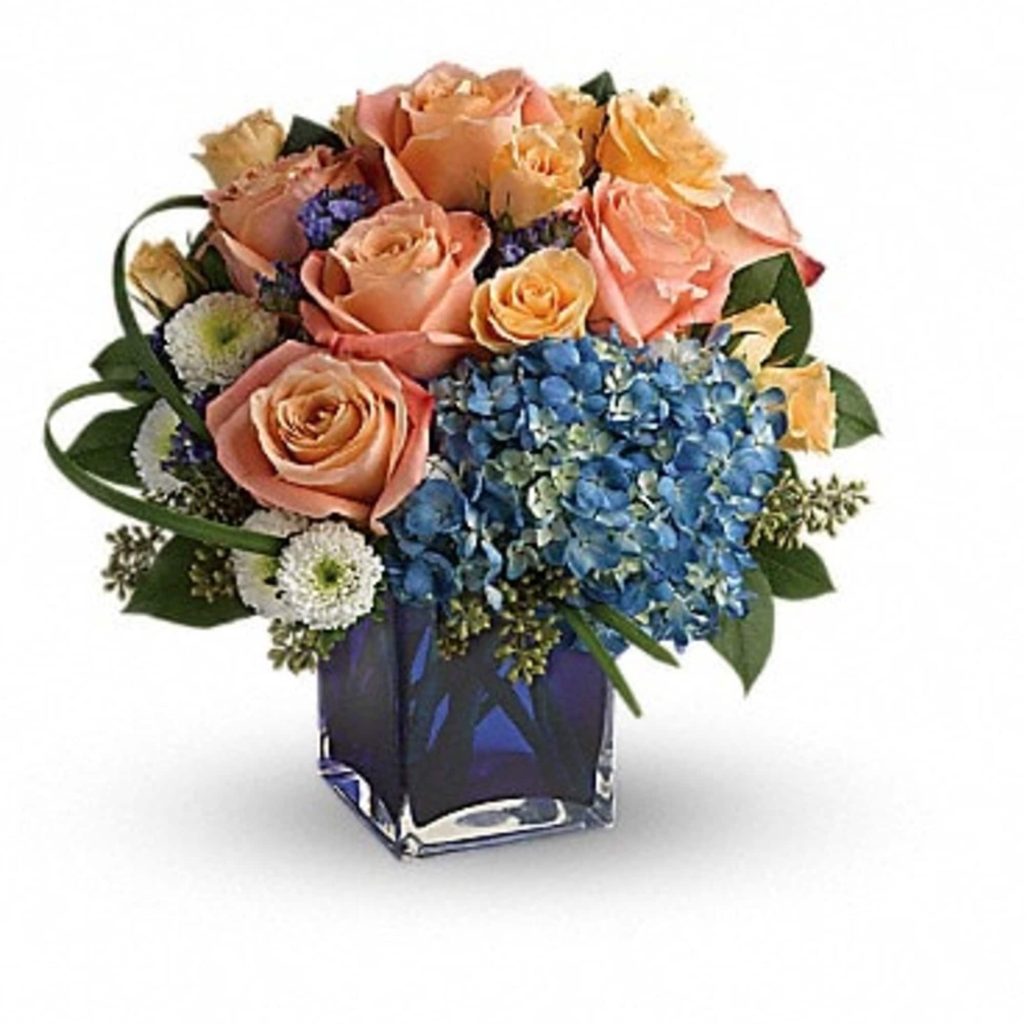 Peach roses and blue hydrangeas in a square glass vase