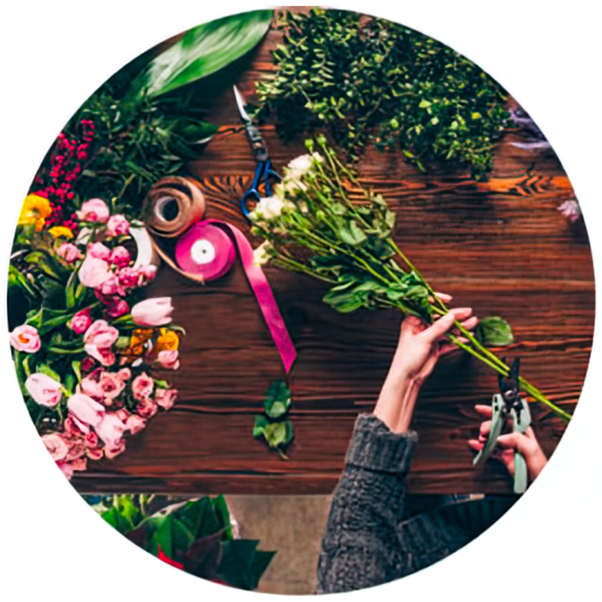 Hands trimming a bouquet of pink flowers on a wooden table