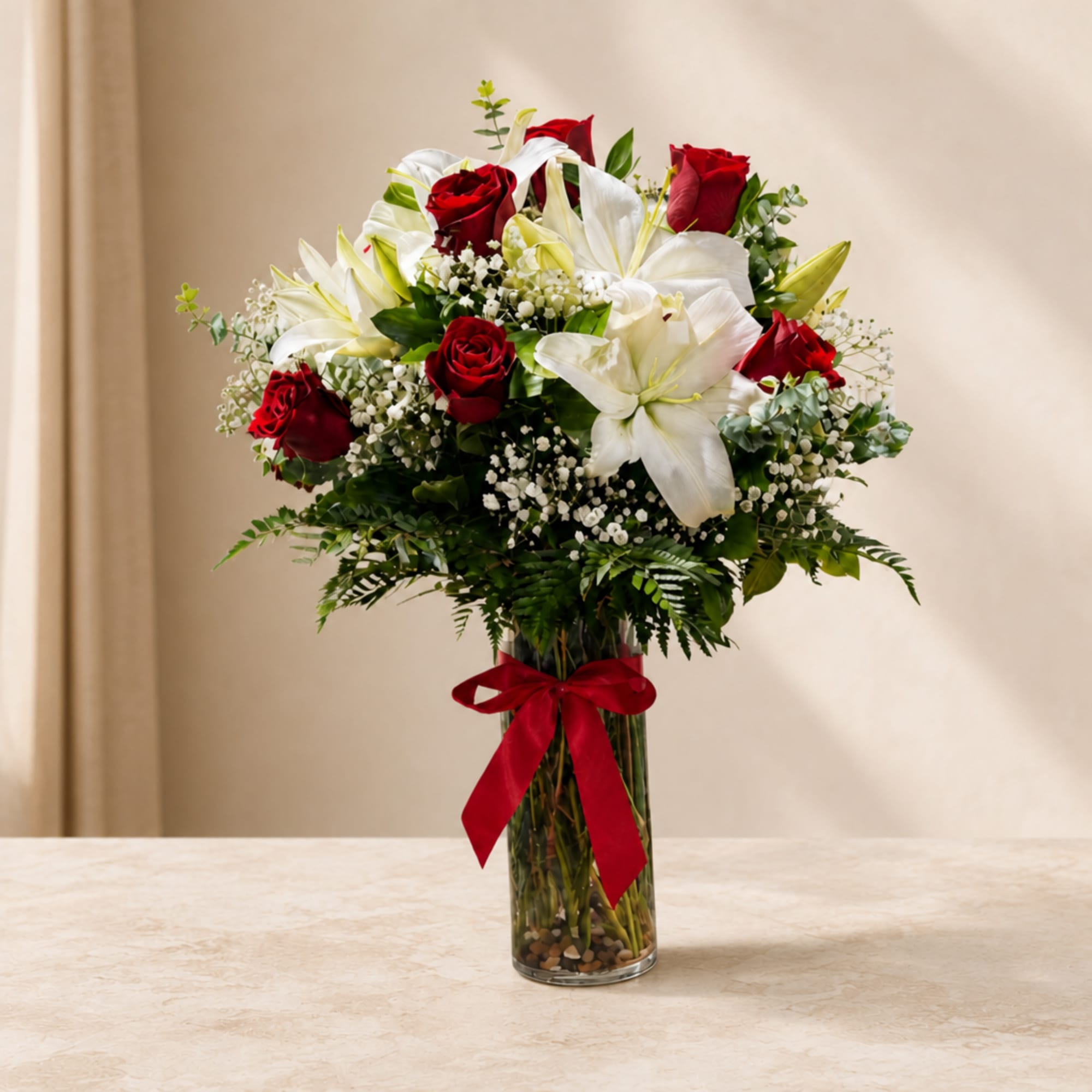 Red roses and white lilies in a clear glass vase with a red ribbon