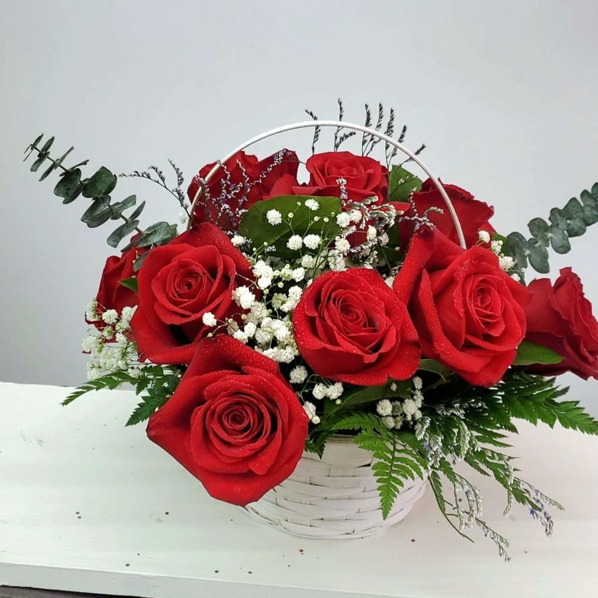 Basket arrangement of red roses with baby's breath and greenery