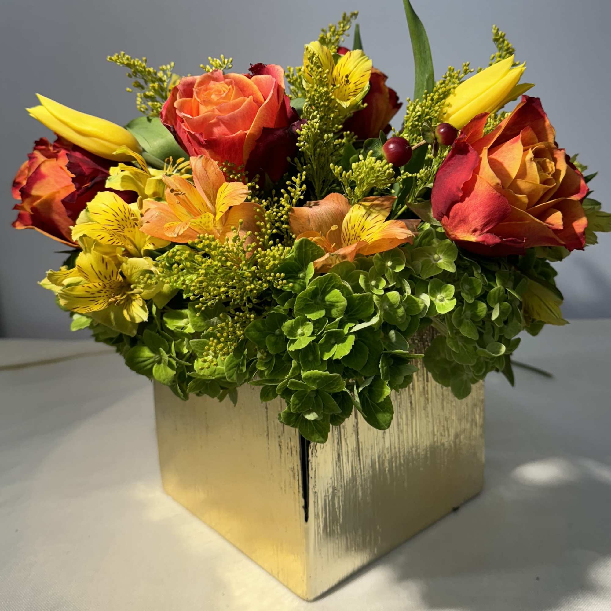 Bouquet of orange and yellow roses in a gold cube vase
