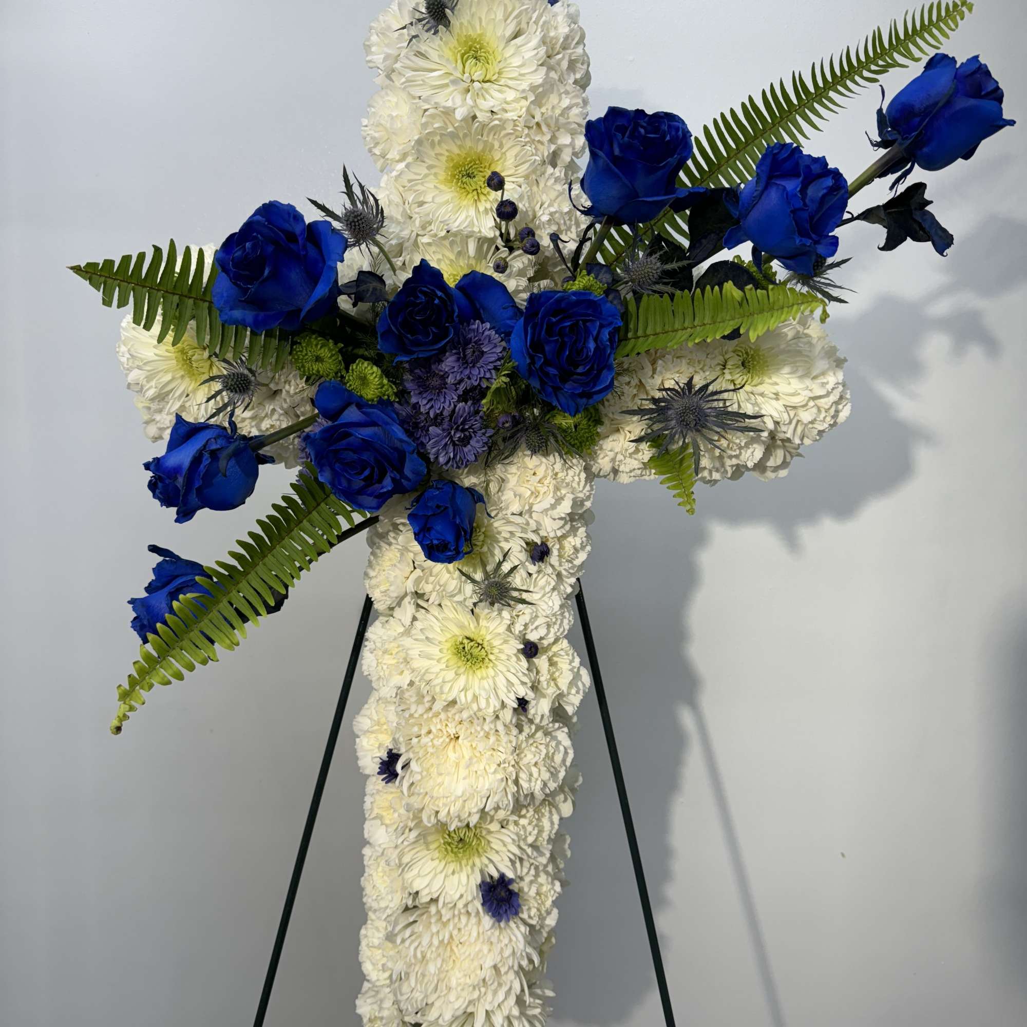 Cross-shaped floral tribute with white chrysanthemums and blue roses on an easel