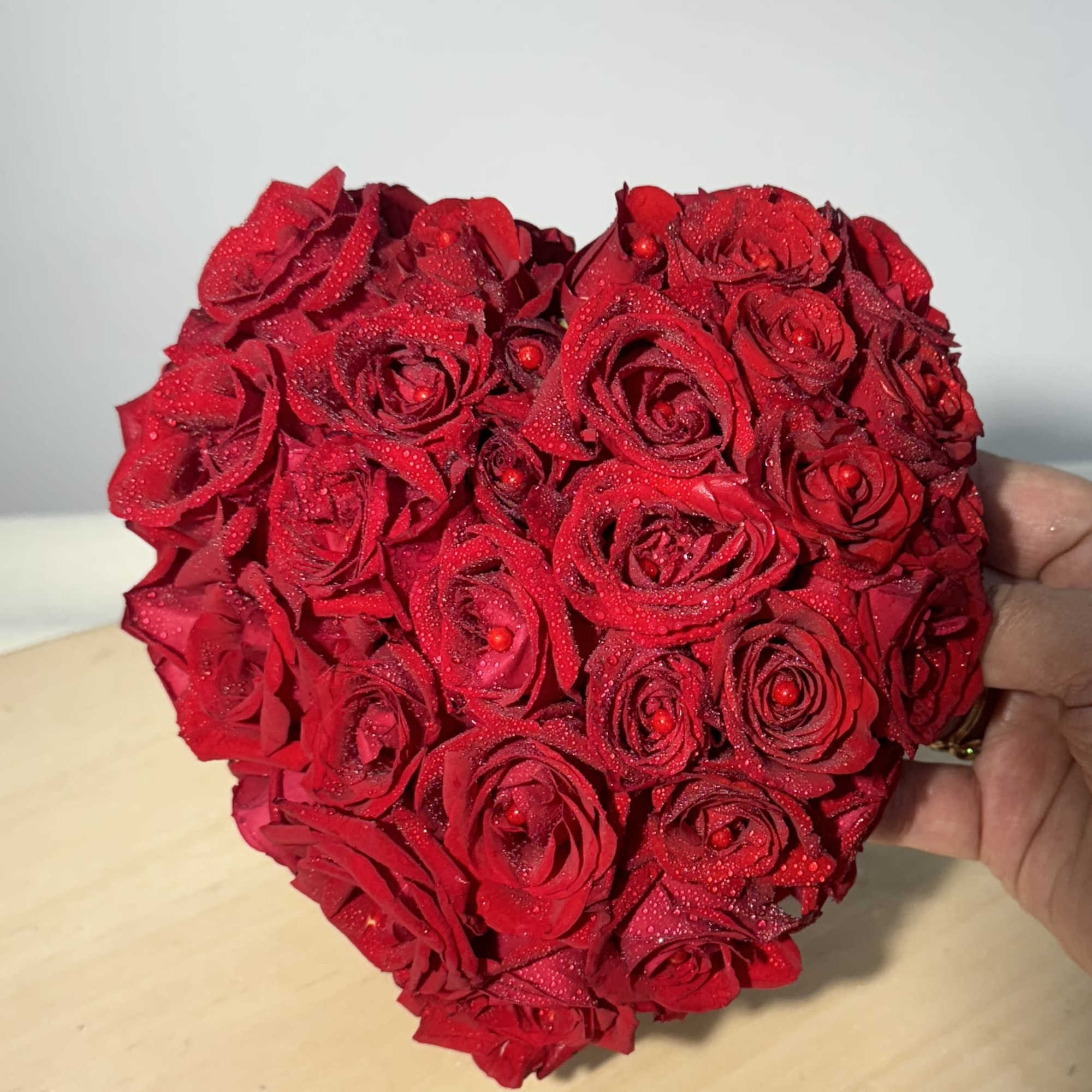 Heart-shaped arrangement of red roses held in a hand