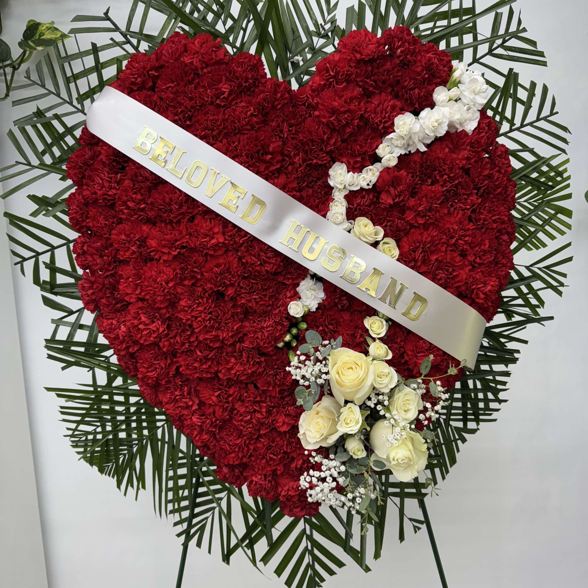Heart-shaped red floral tribute with white roses and a sash reading Beloved Husband