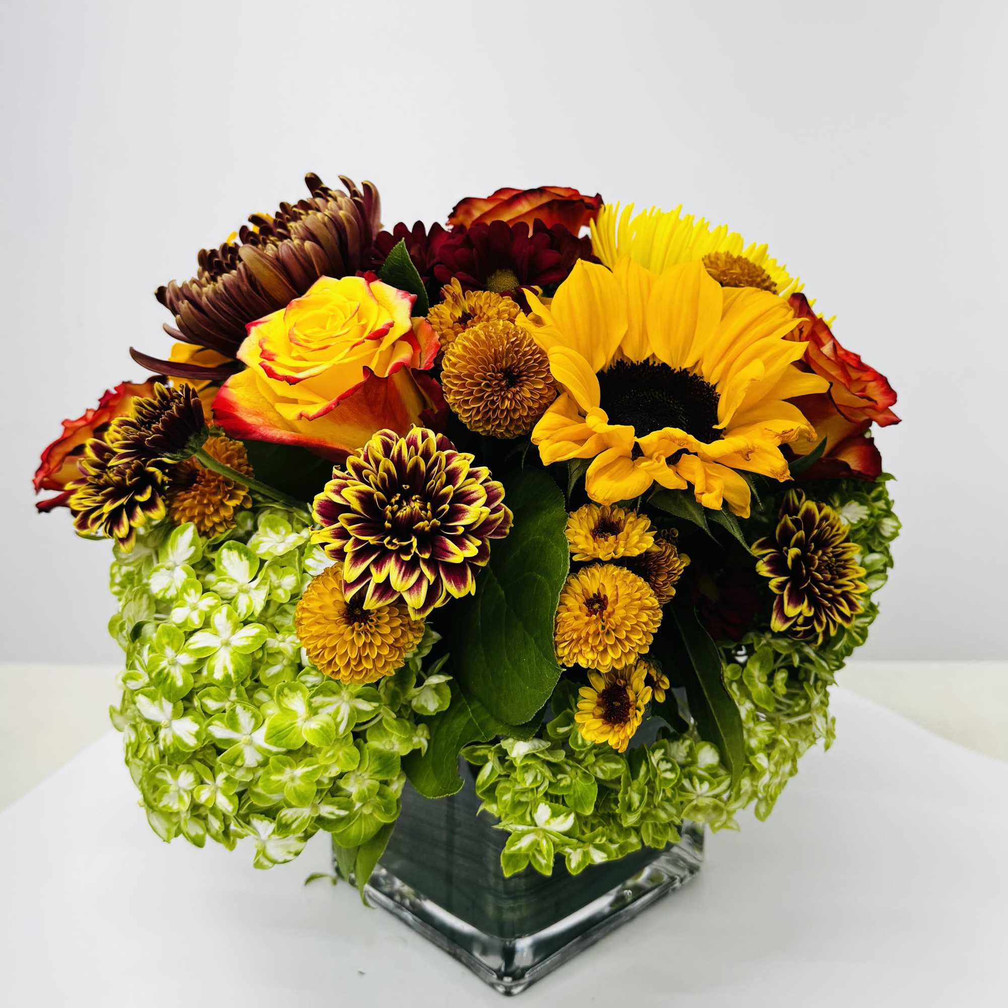 Bouquet of yellow and burgundy flowers in a square glass vase