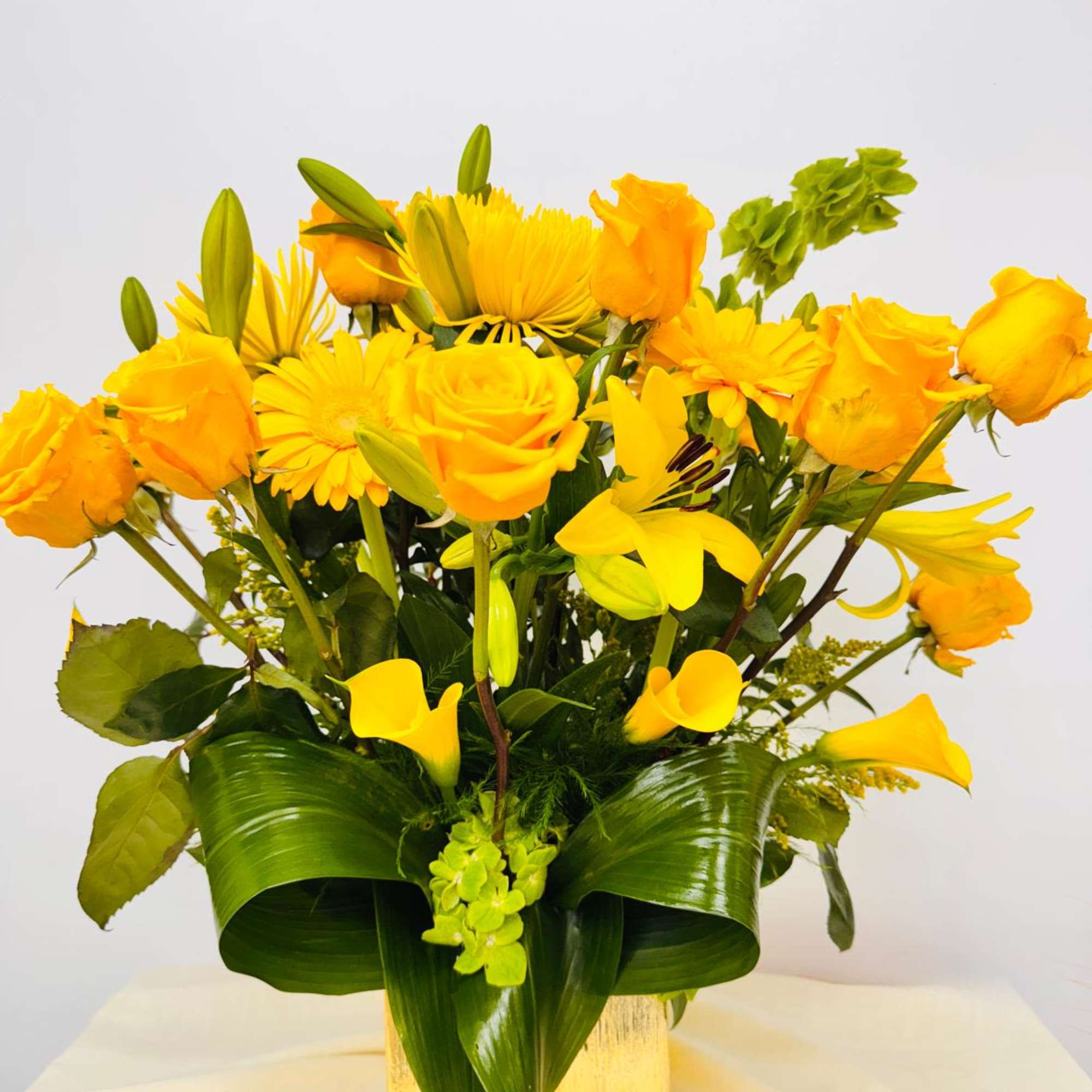 Yellow roses, lilies, and daisies in a square vase