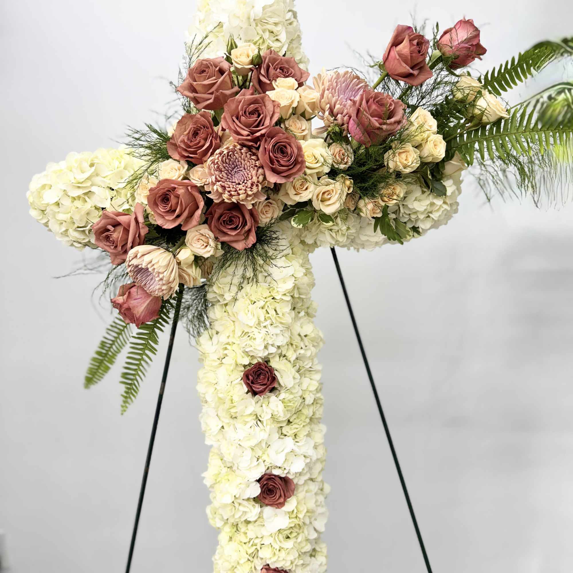 Cross-shaped floral spray with white hydrangeas and pink roses on a stand