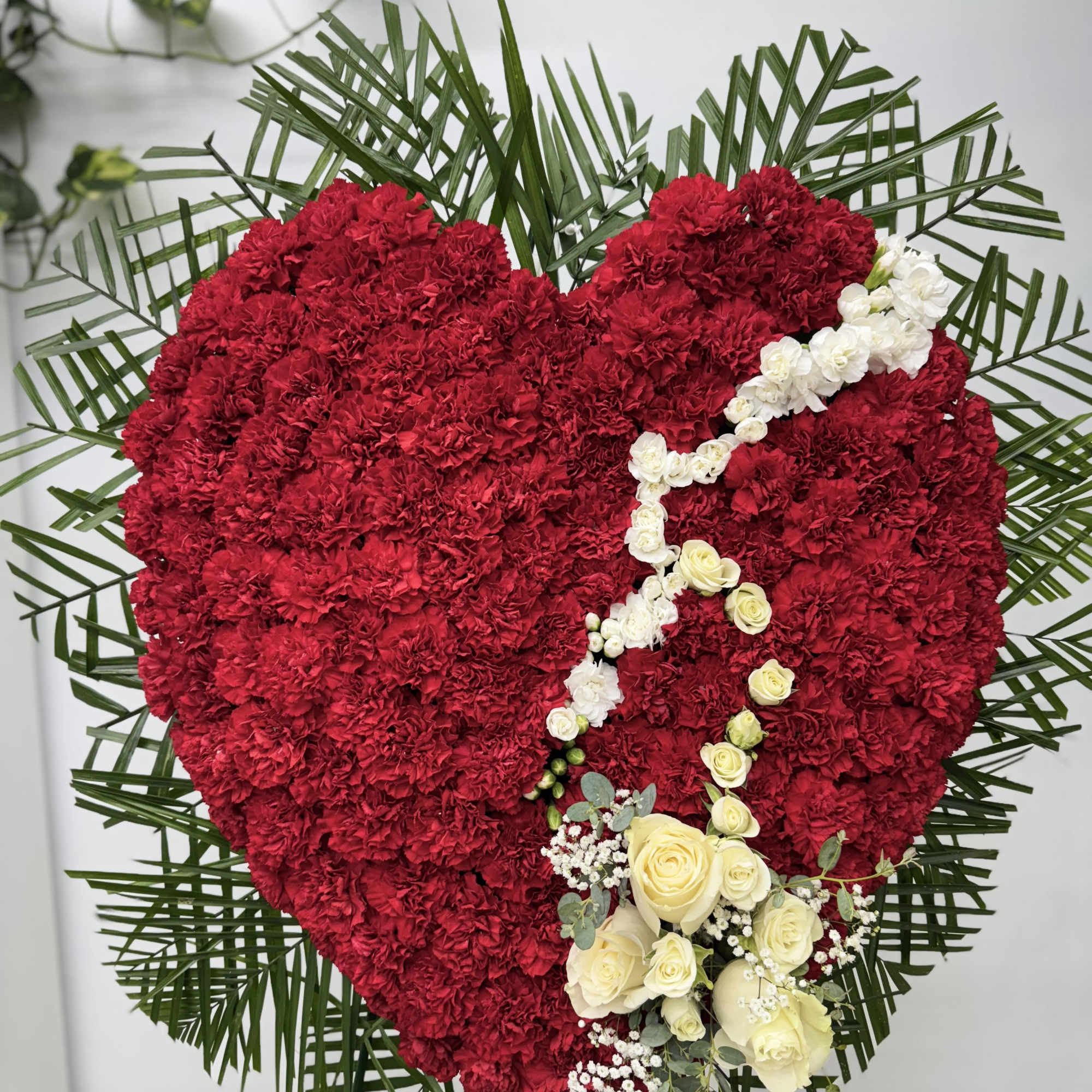 Heart-shaped red floral tribute with white roses and palm fronds