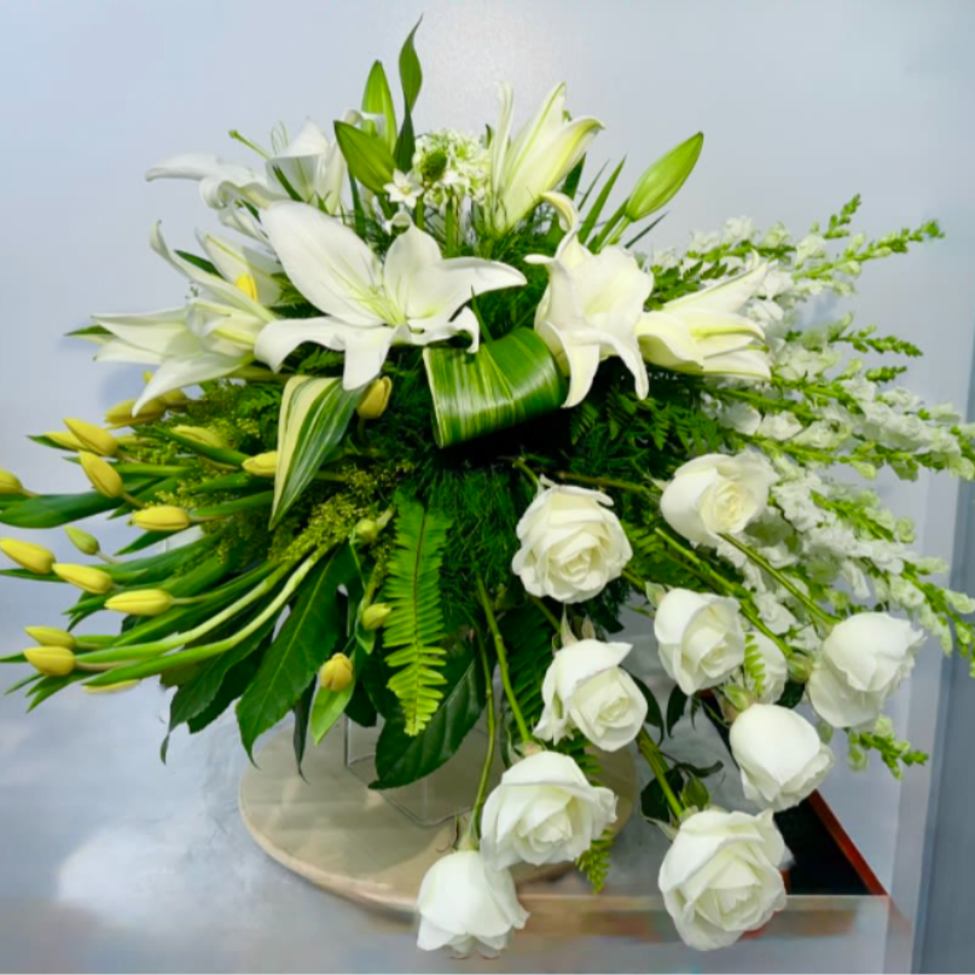 White lilies and roses arranged in a low vase with cascading greenery