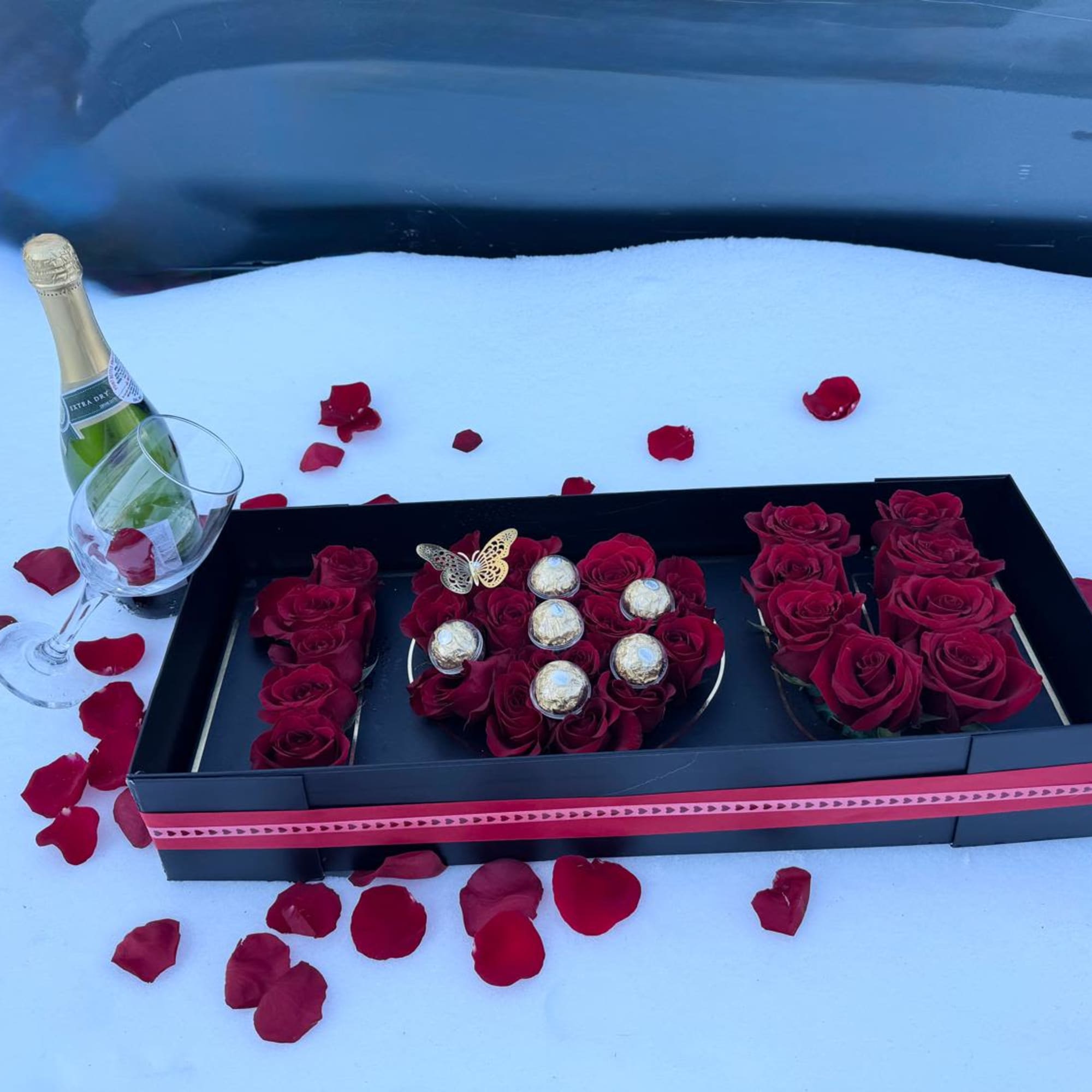 Tray with red roses, chocolates, and a champagne bottle beside a wine glass