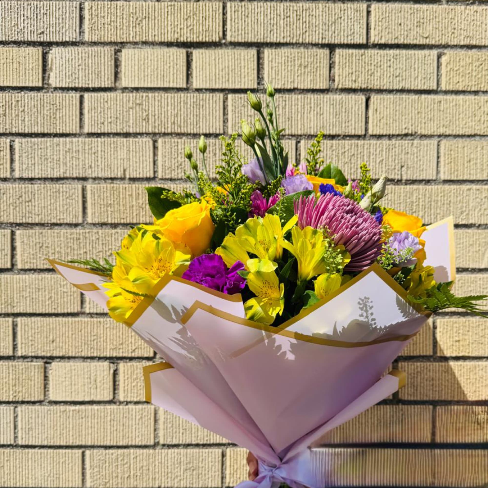 Bouquet of yellow, purple, and pink flowers wrapped in pale paper
