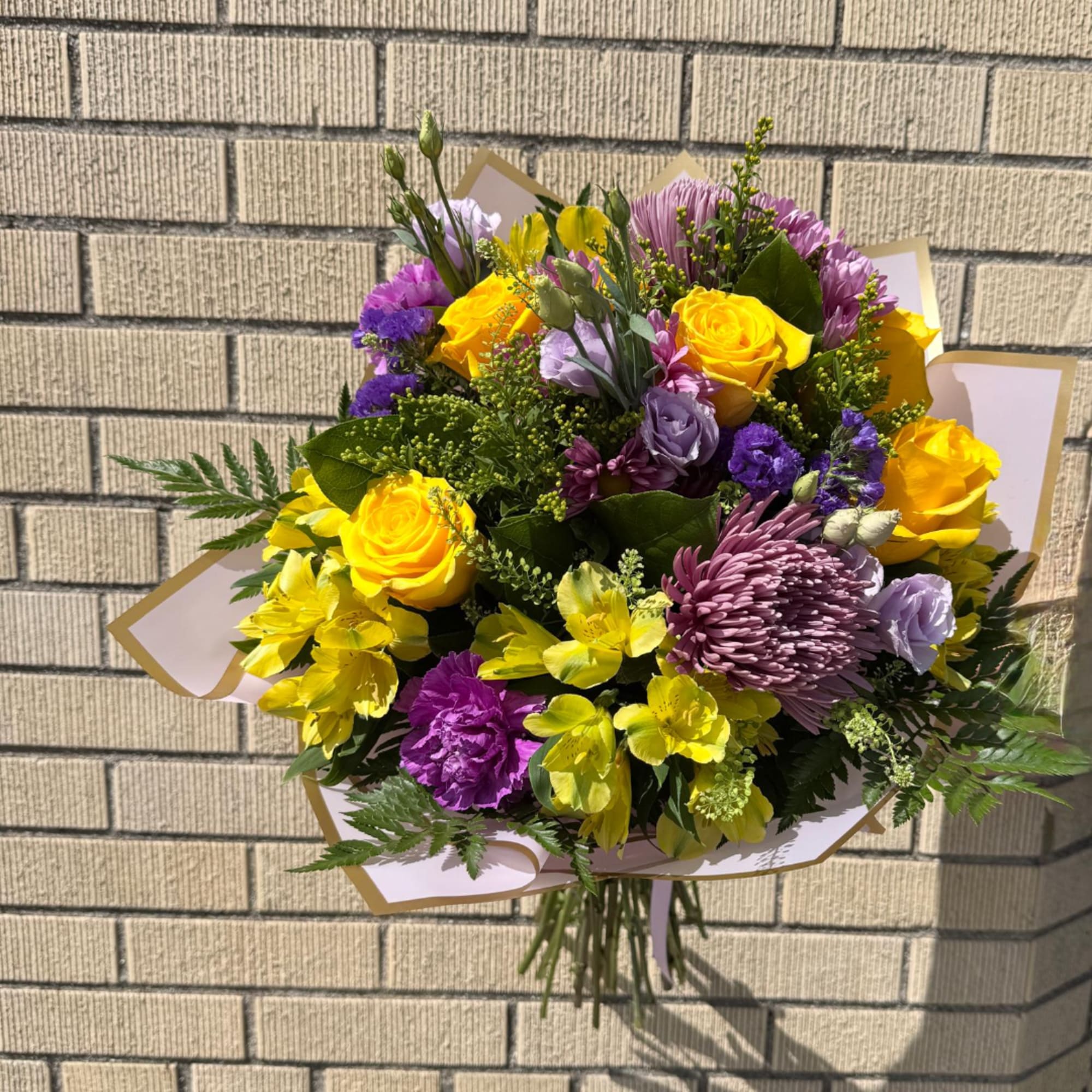 Bouquet of yellow roses, purple blooms, and yellow flowers wrapped in paper