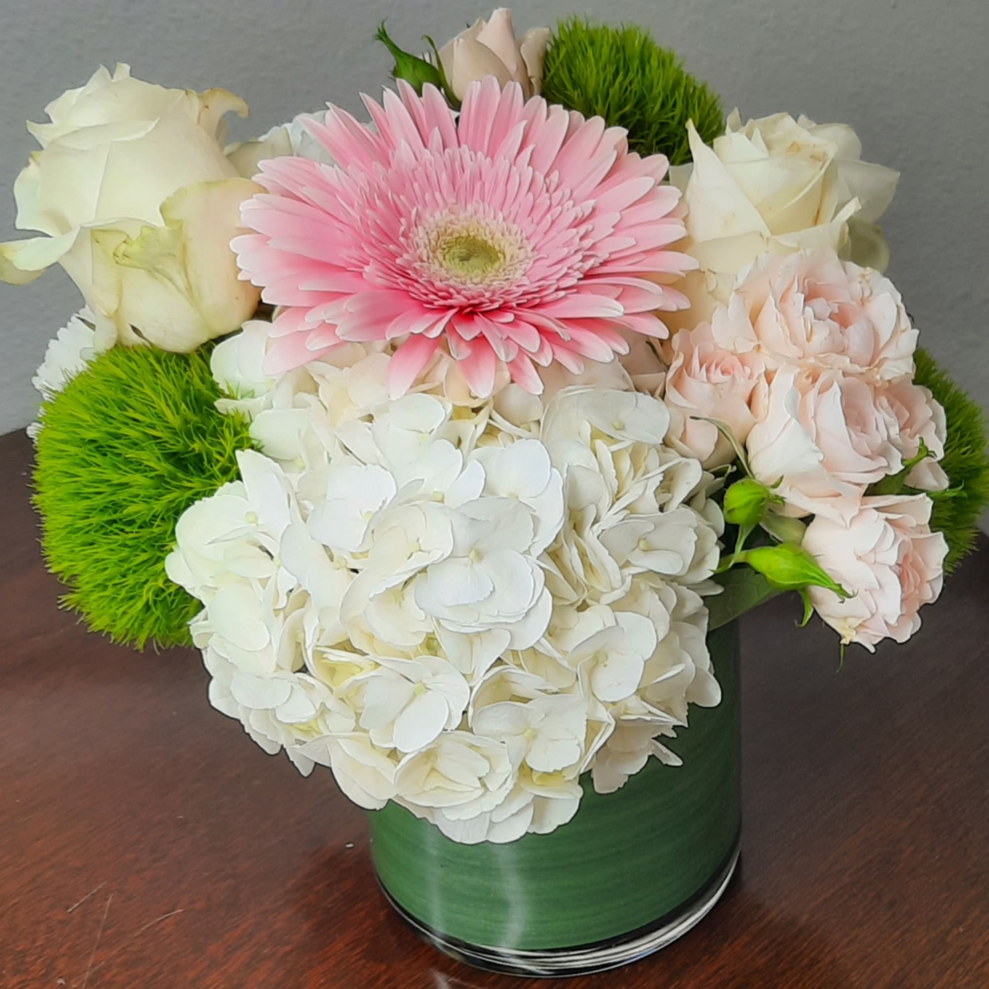 Pink gerbera, white roses, and hydrangeas in a green vase