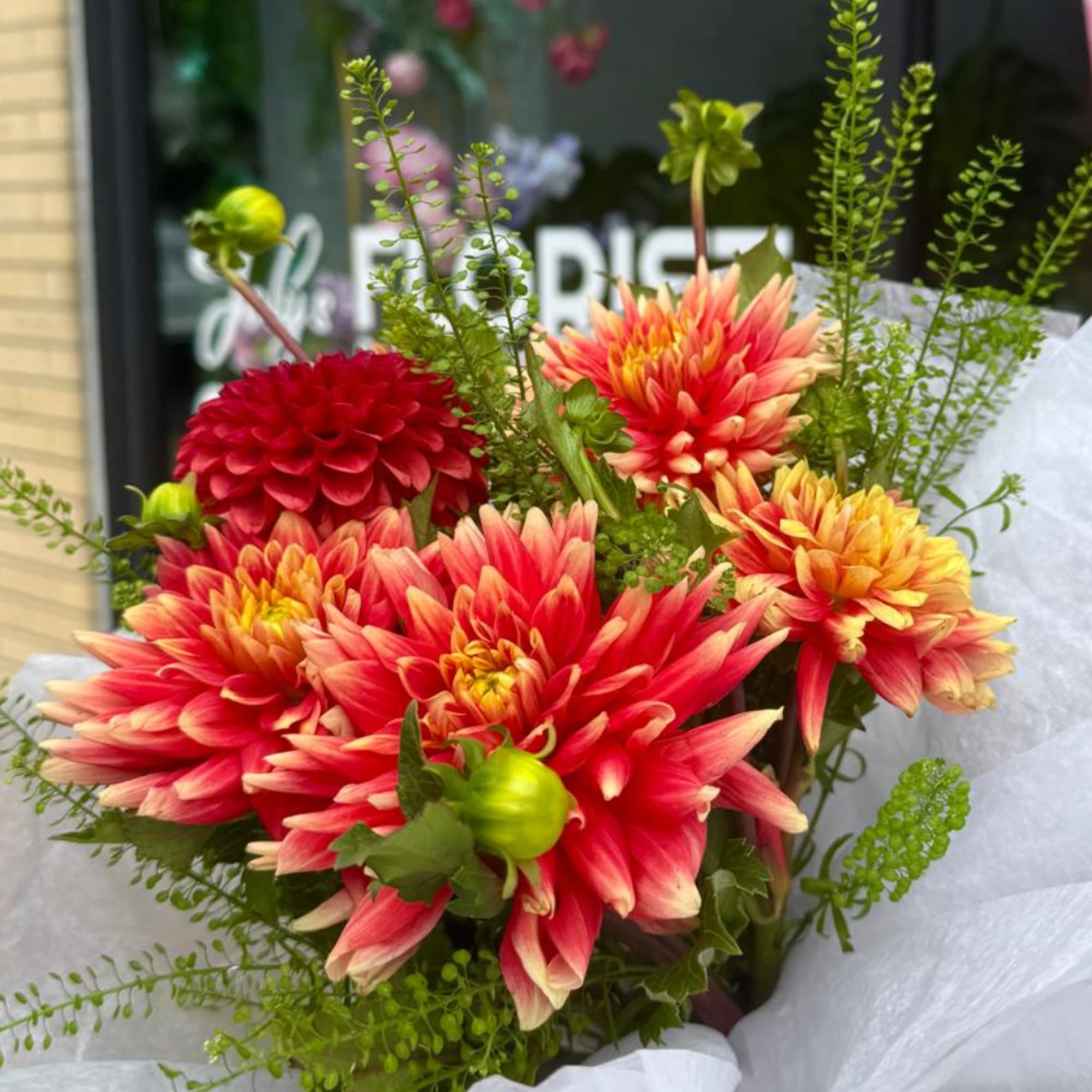 Bouquet of red and yellow dahlias with green filler in white wrap