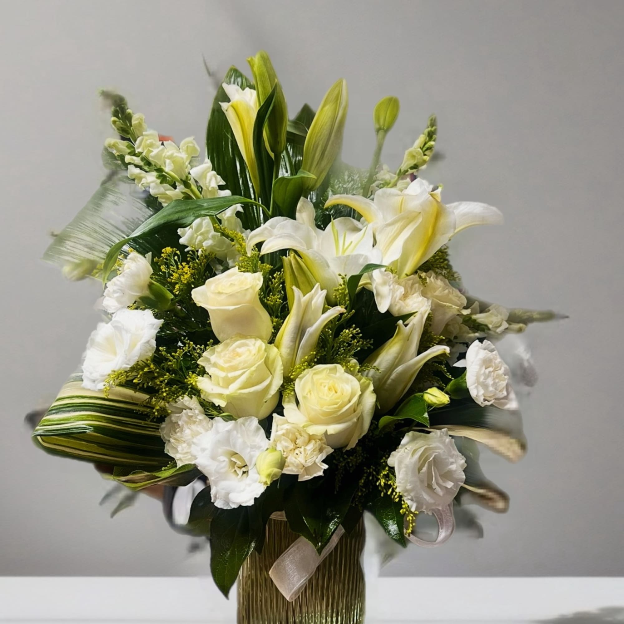 White lilies and roses arranged in a tall vase with green foliage