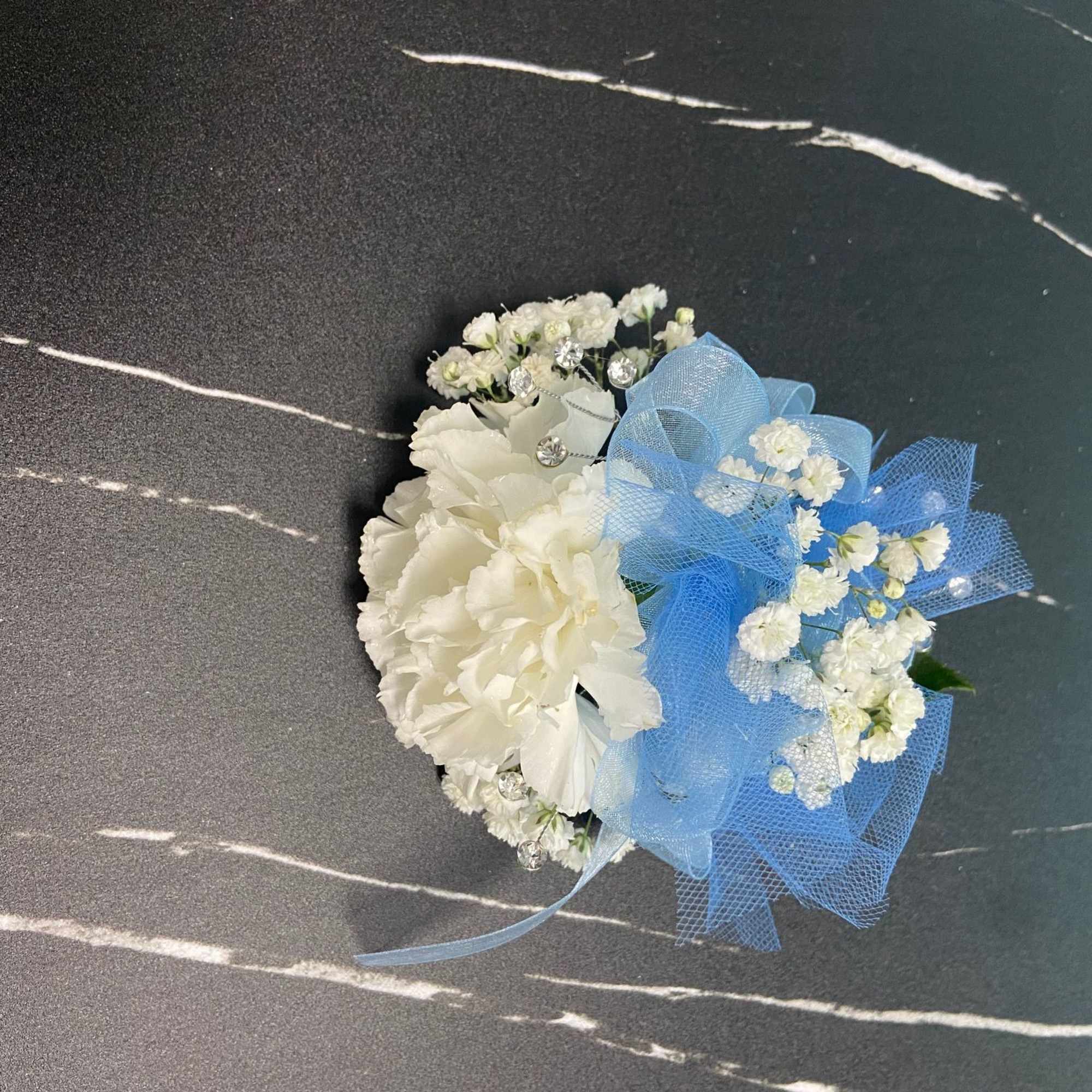 White carnation and small white flowers with a blue mesh bow arranged as a wrist corsage.