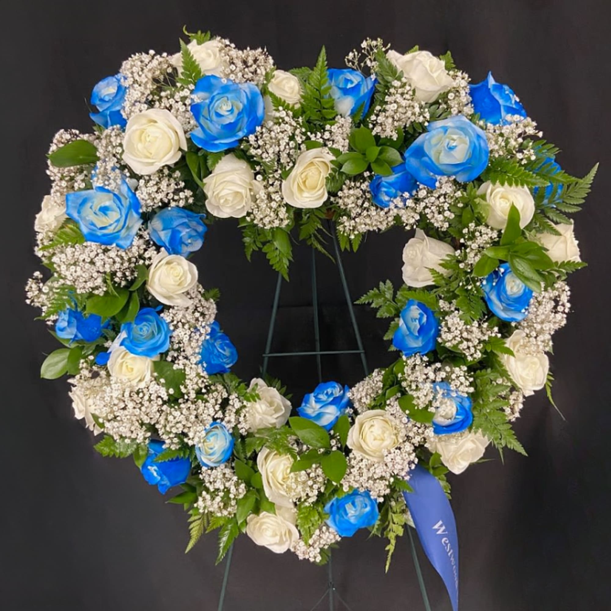 Heart-shaped wreath of blue and white roses on a stand