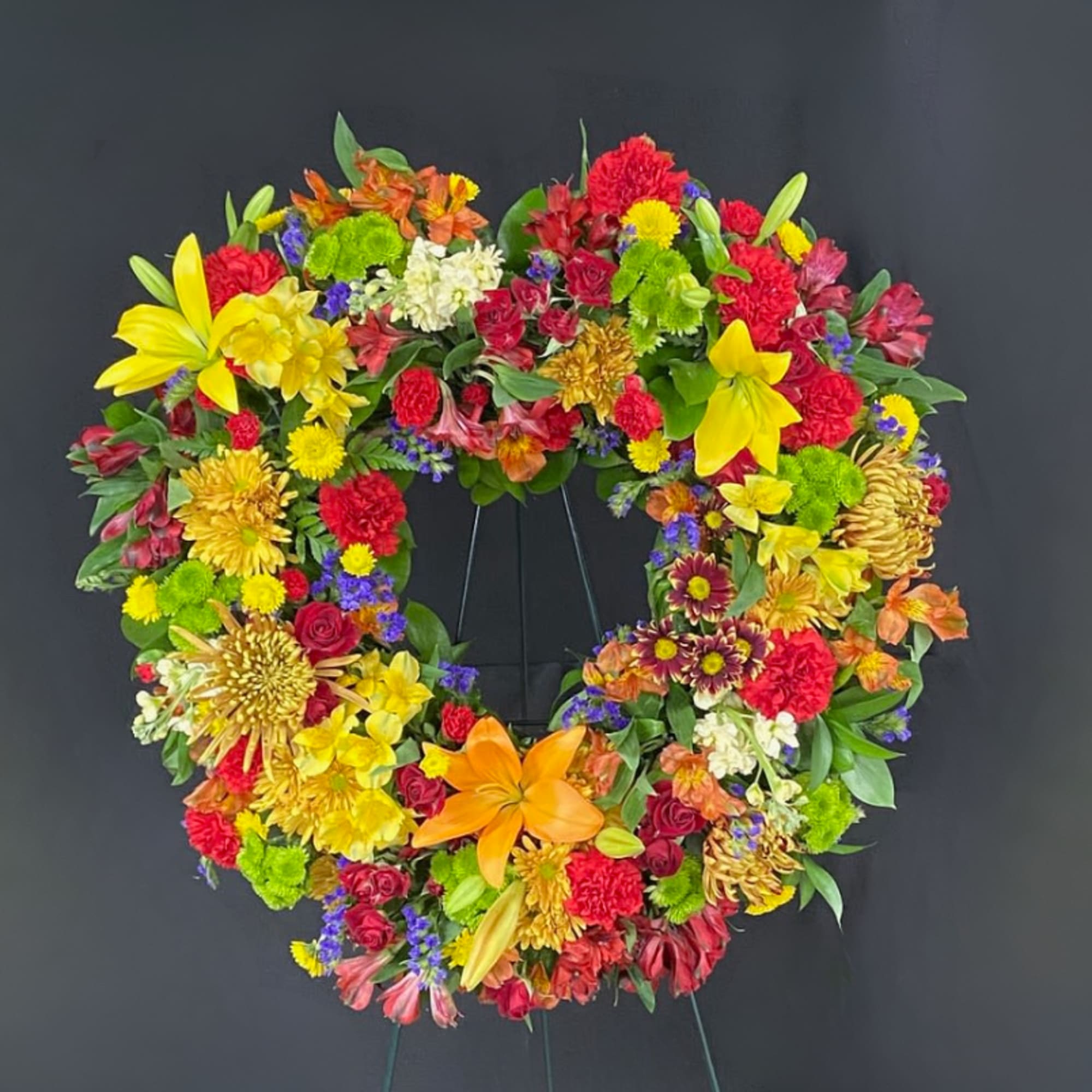 Colorful circular wreath of red, yellow, orange, and purple flowers on a metal stand