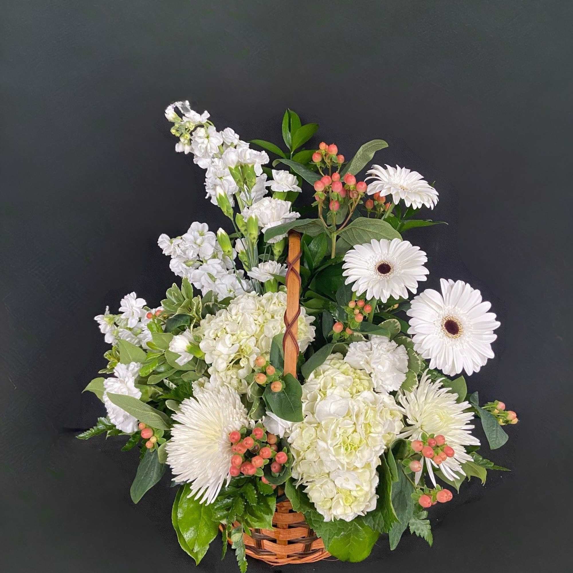 White flowers and pink berries arranged in a wicker basket