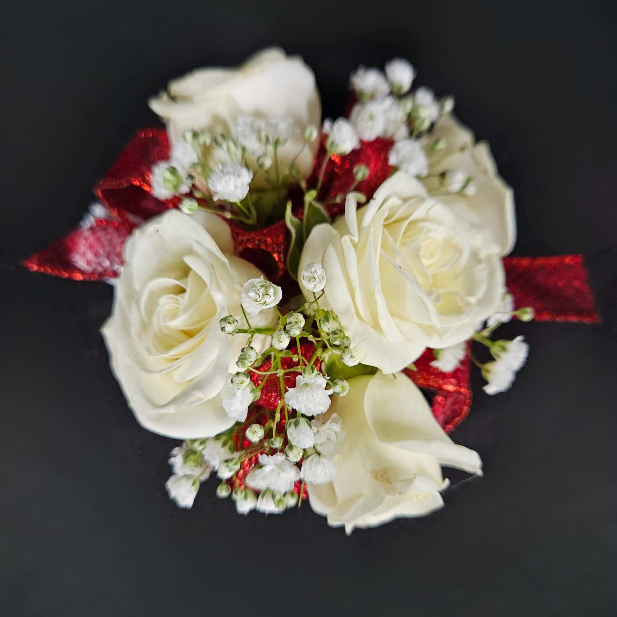 Small cluster of white roses with baby's breath and red ribbon on a dark background