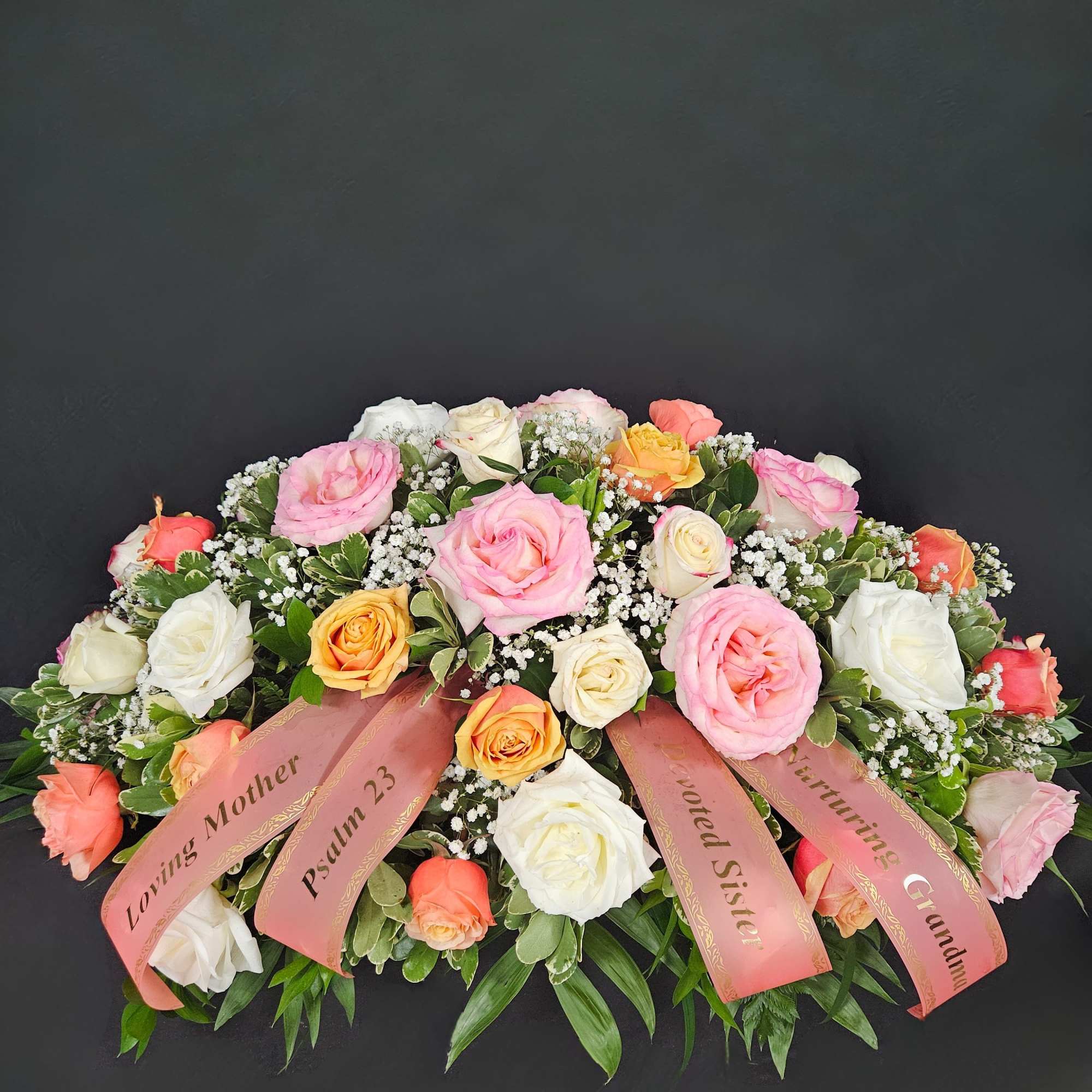 Large pink, white, and peach rose arrangement with ribbons on a dark background