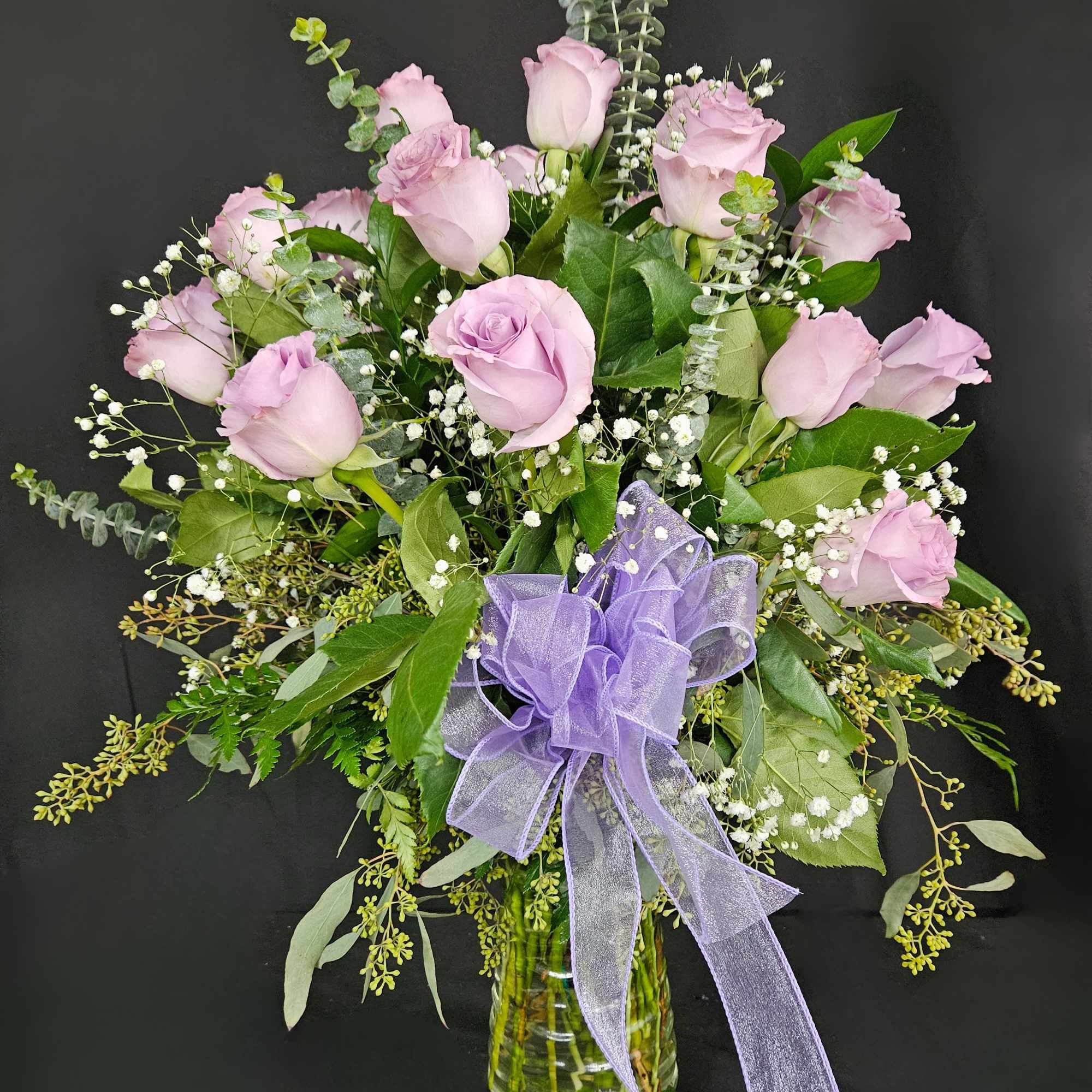 Lavender rose bouquet in a glass vase with a purple ribbon