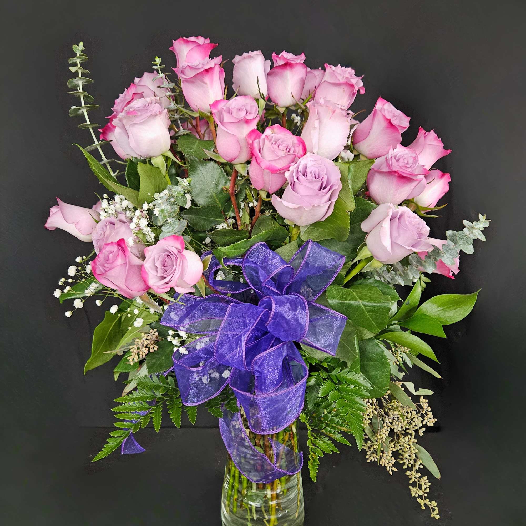 Pink roses in a glass vase with a purple ribbon bow