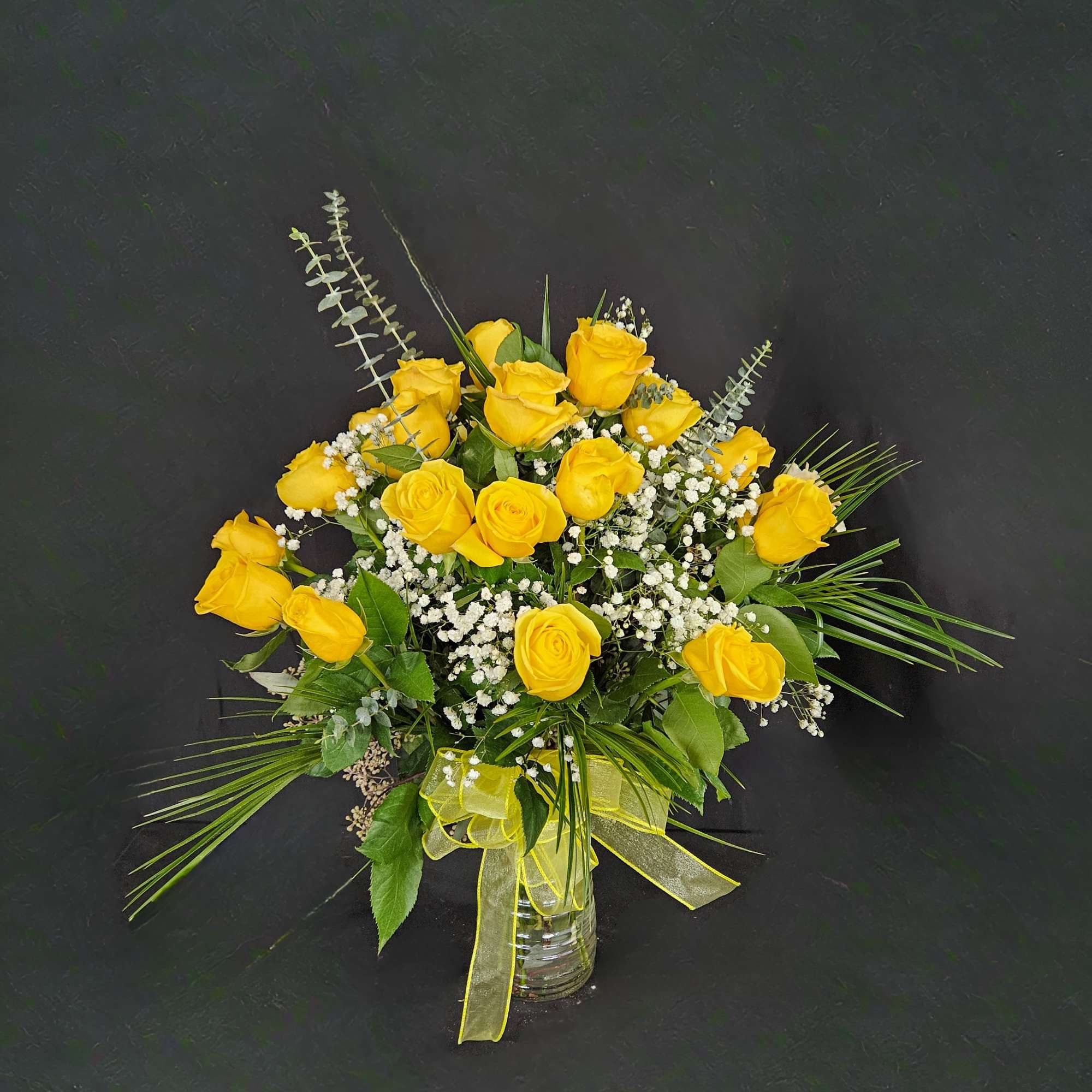 Vase arrangement of yellow roses with white filler flowers and a yellow ribbon bow
