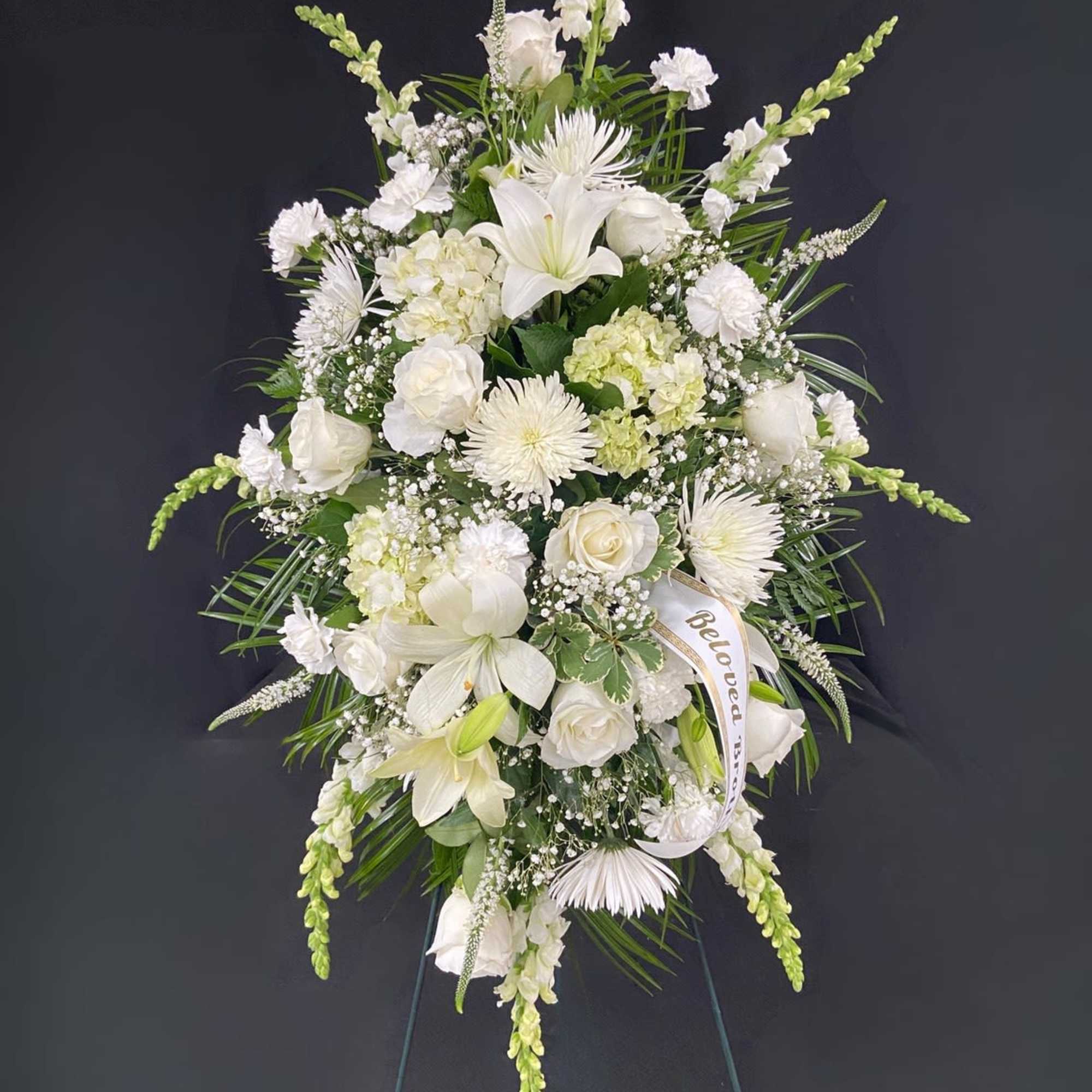 A standing spray of assorted white flowers spread across a bed of