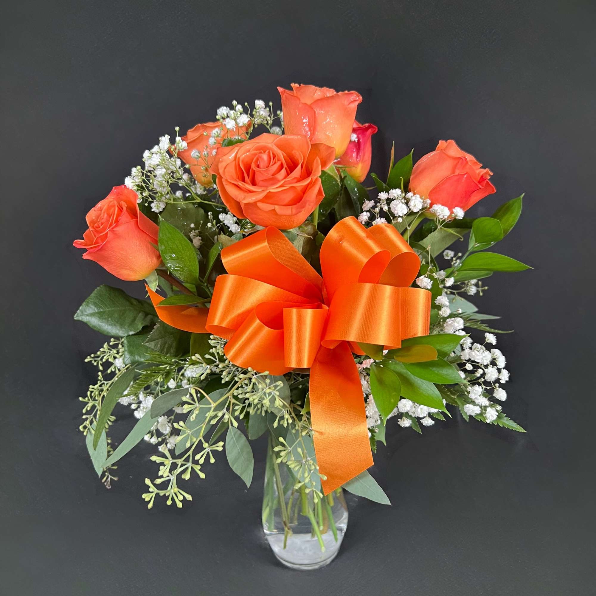 Orange rose bouquet in a clear glass vase with an orange ribbon