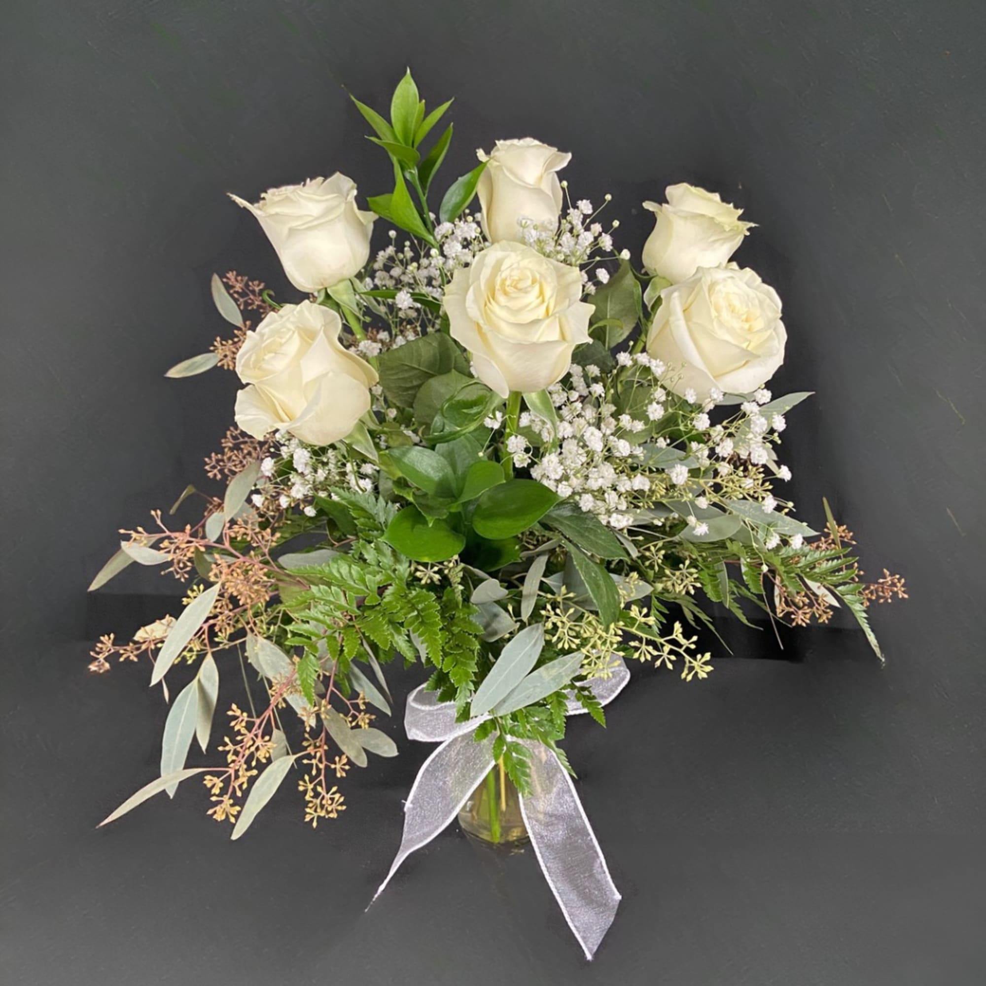 White roses arranged in a glass vase with baby's breath and greenery