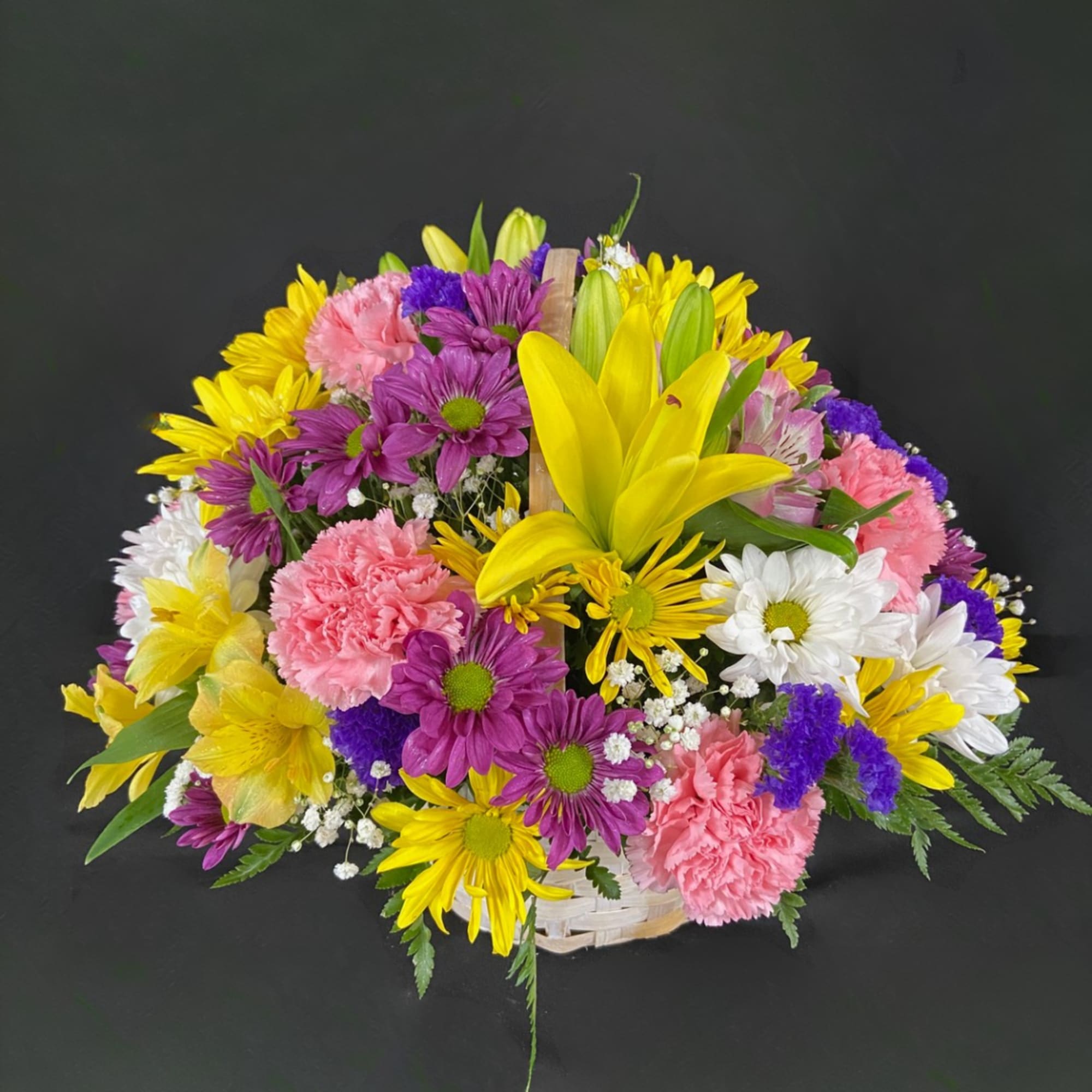 Mixed bouquet of yellow lilies, purple daisies, pink carnations, and white daisies in a basket