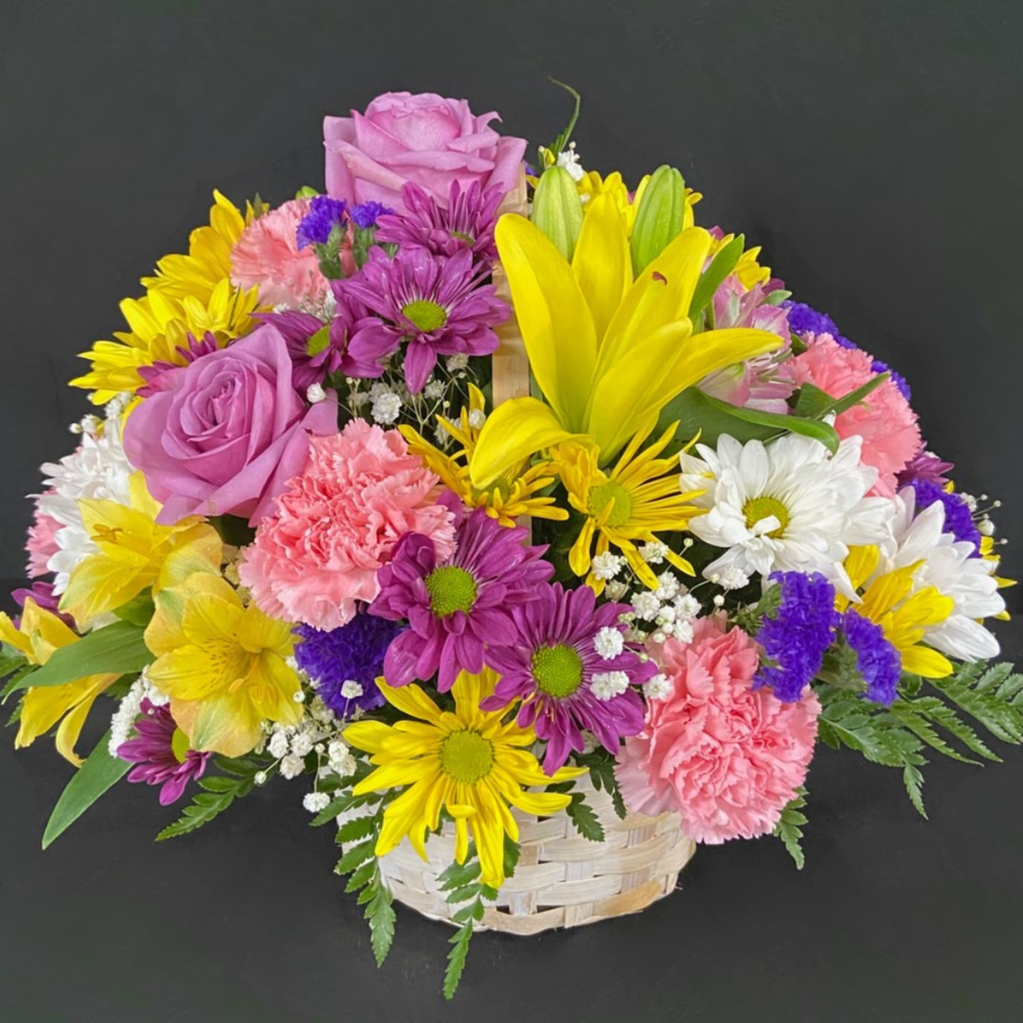 Mixed bouquet in a white basket with pink, yellow, purple, and white flowers