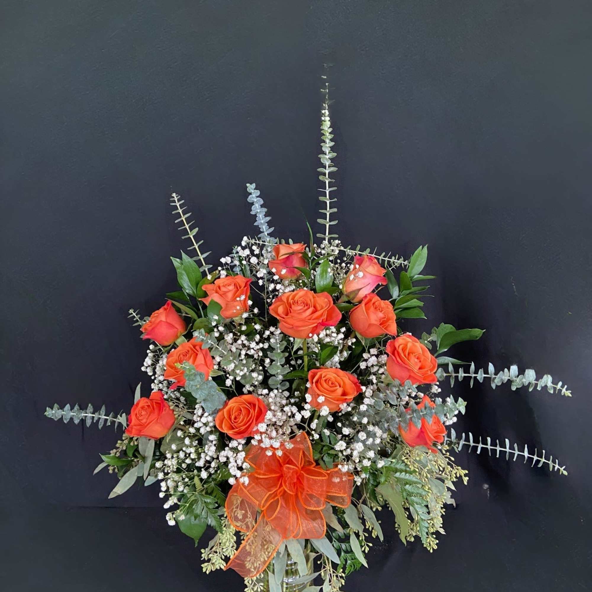 Orange rose arrangement in a clear glass vase with baby's breath and greenery