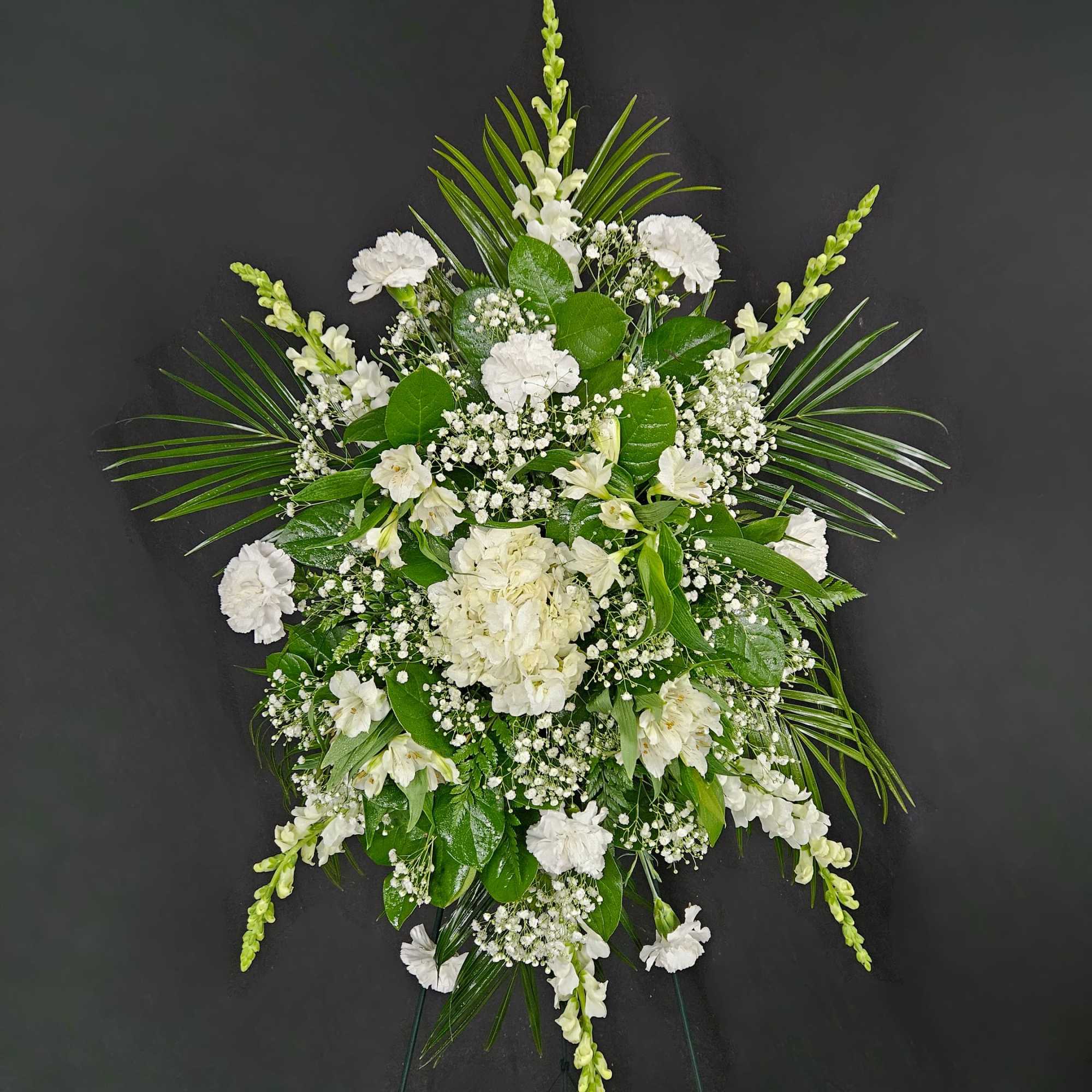 A standing spray of assorted white flowers spread across a bed of